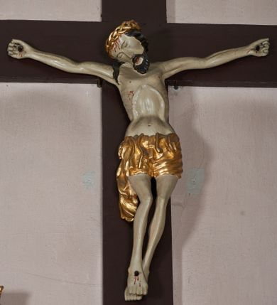 Zdjęcie nr 1: W centrum postać zmarłego Chrystusa, przybitego trzema gwoździami do krzyża. Postać w delikatnym zwisie, o szeroko rozłożonych ramionach i delikatnie przegiętej sylwetce. Duża głowa w koronie cierniowej opada na prawe ramię; twarz o sumarycznych rysach, okolona zarostem; włosy w postaci pukli opadają na ramię. Ciało naprężone, wychudzone, ekspresyjnie kształtowane, uwypuklone poszczególne elementy anatomiczne, z zaznaczonymi śladami męki. Perizonium w formie tkaniny ściśle opasującej biodra, drapowanej w spływające faliście fałdy, ze zwisem na prawym boku. Titulus w formie banderoli z napisem „INRI”.Po lewej stronie figura św. Elżbiety, zwróconej frontalnie z wyciągniętymi przed siebie rękami. Twarz pełna, niezindywidualizowana. Na nakrytej welonem głowie ma koronę. Postać ubrana w błękitną tunikę przepasaną w talii złotą szarfą i podwikę; na ramiona ma narzucony czerwony płaszcz. Po prawej postać św. Katarzyny Sieneńskiej w analogicznym układzie ciała. Twarz pełna, również niezindywidualizowana. Święta jest ubrana w habit dominikański. Karnacja postaci bardzo jasna. 