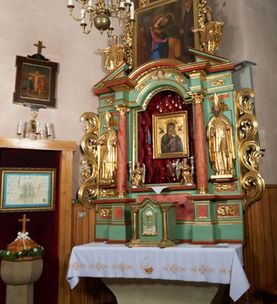 Zdjęcie nr 2: Ołtarz przyścienny, architektoniczny, trójosiowy, jednokondygnacyjny ze zwieńczeniem i uszakami. Mensa w typie sarkofagowym na niewielkim prostopadłościennym postumencie. Tabernakulum drewniane, architektoniczne, ujęte złoconymi kolumienkami dźwigającymi wyłamane i wyniesione belkowanie. Na drzwiczkach płaskorzeźbione przedstawienie kielicha z hostią. Nastawa drewniana ujęta korynckimi kolumnami ustawionymi na wysokich postumentach. Dźwigają one pełne, wyłamane na osiach kolumn i półkoliście wyniesione na osi środkowej ołtarza belkowanie. Fryz dekorowany rozetami oraz uskrzydloną główką anielską. Powyżej odcinki przyczółka, na których ustawione pełnoplastyczne figury świętych wojowników. W polu środkowym nisza zamknięta łukiem półkolistym nadwieszonym mieszcząca obraz Matki Boskiej Nieustającej Pomocy. W osiach bocznych ustawione na tle płycin pełnoplastyczne figury świętych biskupów w złoconych szatach oraz akantowe, ażurowe uszaki utworzone z wici akantowej. W zwieńczeniu obraz „Nawiedzenie Najświętszej Marii Panny” w kształcie stojącego prostokąta ujęty ażurowymi uszami utworzonymi z ornamentu mażowinowo-chrząstkowego, i winorośli. Powyżej, analogicznie, mniejszy obraz „Trójca Święta” w kształcie prostokąta stojącego o ściętych górnych narożach, zwieńczonego krzyżem równoramiennym. Struktura ołtarza w kolorze jasnozielonym, wypełnienia płycin, trzony kolumn oraz elementy gzymsu jasnoczerwone, marmoryzowane; ornamenty złocone.