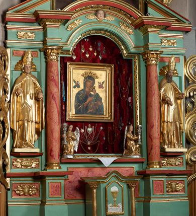 Zdjęcie nr 4: Ołtarz przyścienny, architektoniczny, trójosiowy, jednokondygnacyjny ze zwieńczeniem i uszakami. Mensa w typie sarkofagowym na niewielkim prostopadłościennym postumencie. Tabernakulum drewniane, architektoniczne, ujęte złoconymi kolumienkami dźwigającymi wyłamane i wyniesione belkowanie. Na drzwiczkach płaskorzeźbione przedstawienie kielicha z hostią. Nastawa drewniana ujęta korynckimi kolumnami ustawionymi na wysokich postumentach. Dźwigają one pełne, wyłamane na osiach kolumn i półkoliście wyniesione na osi środkowej ołtarza belkowanie. Fryz dekorowany rozetami oraz uskrzydloną główką anielską. Powyżej odcinki przyczółka, na których ustawione pełnoplastyczne figury świętych wojowników. W polu środkowym nisza zamknięta łukiem półkolistym nadwieszonym mieszcząca obraz Matki Boskiej Nieustającej Pomocy. W osiach bocznych ustawione na tle płycin pełnoplastyczne figury świętych biskupów w złoconych szatach oraz akantowe, ażurowe uszaki utworzone z wici akantowej. W zwieńczeniu obraz „Nawiedzenie Najświętszej Marii Panny” w kształcie stojącego prostokąta ujęty ażurowymi uszami utworzonymi z ornamentu mażowinowo-chrząstkowego, i winorośli. Powyżej, analogicznie, mniejszy obraz „Trójca Święta” w kształcie prostokąta stojącego o ściętych górnych narożach, zwieńczonego krzyżem równoramiennym. Struktura ołtarza w kolorze jasnozielonym, wypełnienia płycin, trzony kolumn oraz elementy gzymsu jasnoczerwone, marmoryzowane; ornamenty złocone.