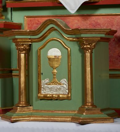 Zdjęcie nr 13: Ołtarz przyścienny, architektoniczny, trójosiowy, jednokondygnacyjny ze zwieńczeniem i uszakami. Mensa w typie sarkofagowym na niewielkim prostopadłościennym postumencie. Tabernakulum drewniane, architektoniczne, ujęte złoconymi kolumienkami dźwigającymi wyłamane i wyniesione belkowanie. Na drzwiczkach płaskorzeźbione przedstawienie kielicha z hostią. Nastawa drewniana ujęta korynckimi kolumnami ustawionymi na wysokich postumentach. Dźwigają one pełne, wyłamane na osiach kolumn i półkoliście wyniesione na osi środkowej ołtarza belkowanie. Fryz dekorowany rozetami oraz uskrzydloną główką anielską. Powyżej odcinki przyczółka, na których ustawione pełnoplastyczne figury świętych wojowników. W polu środkowym nisza zamknięta łukiem półkolistym nadwieszonym mieszcząca obraz Matki Boskiej Nieustającej Pomocy. W osiach bocznych ustawione na tle płycin pełnoplastyczne figury świętych biskupów w złoconych szatach oraz akantowe, ażurowe uszaki utworzone z wici akantowej. W zwieńczeniu obraz „Nawiedzenie Najświętszej Marii Panny” w kształcie stojącego prostokąta ujęty ażurowymi uszami utworzonymi z ornamentu mażowinowo-chrząstkowego, i winorośli. Powyżej, analogicznie, mniejszy obraz „Trójca Święta” w kształcie prostokąta stojącego o ściętych górnych narożach, zwieńczonego krzyżem równoramiennym. Struktura ołtarza w kolorze jasnozielonym, wypełnienia płycin, trzony kolumn oraz elementy gzymsu jasnoczerwone, marmoryzowane; ornamenty złocone.