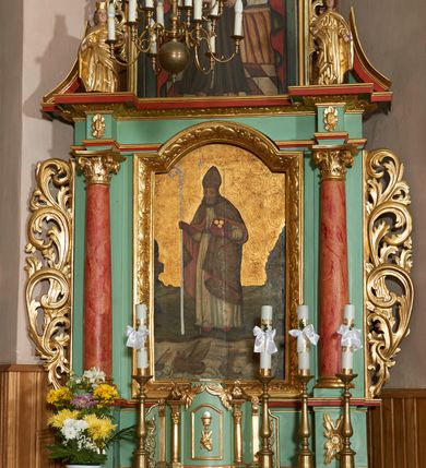 Zdjęcie nr 13: Ołtarz przyścienny, architektoniczny, jednoosiowy, jednokondygnacyjny ze zwieńczeniem; uszaty. Mensa w typie sarkofagowym na niewielkim prostopadłościennym postumencie. Tabernakulum drewniane, architektoniczne, ujęte parami złoconych kolumienek, na osi których odcinki belkowania i spiralnie zwinięte akantowe woluty oraz kanelowanymi pilastrami. W zwieńczeniu motyw podwieszonej kotary oraz lambrekin. Na drzwiczkach płaskorzeźbione przedstawienie kielicha z hostią. Nastawa drewniana, ujęta korynckimi kolumnami ustawionymi na wysokich postumentach zdobionych plakietami roślinnymi. Dźwigają one pełne, wyłamane na ich osiach belkowanie. Fryz wysuniętych części dekorowany rozetami, silnie wystający gzyms zdobiony akantem. Powyżej odcinki przyczółka, na tle których ustawione pełnoplastyczne figury świętych dziewic w koronach i złoconych szatach. W kondygnacji pierwszej nisza zamknięta łukiem półkolistym nadwieszonym, mieszcząca obraz św. Mikołaja. Kondygnacja ujęta ażurowymi akantowymi uszakami. W zwieńczeniu przedstawienie św. Antoniego Padewskiego w formie stojącego prostokąta, ujętego ażurowymi uszakami utworzonymi z wici akantu. Powyżej, analogicznie, mniejsze ujęcie Boga Ojca w kształcie stojącego prostokąta o ściętych górnych narożach, zwieńczonego krzyżem równoramiennym. Struktura ołtarza w kolorze jasnozielonym, wypełnienia płycin, trzony kolumn oraz elementy gzymsu jasnoczerwone; ornamenty złocone.