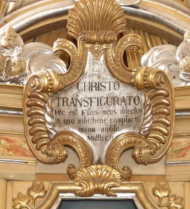 Zdjęcie nr 7: Ołtarz architektoniczny, jednokondygnacyjny, jednoosiowy, ze zwieńczeniem. Nastawa zbudowana na kamiennym, wysokim cokole, lekko wklęsła, ujęta zwielokrotnionymi pilastrami kompozytowymi o kanelowanych trzonach i zewnętrznymi, nieznacznie cofniętymi kolumnami, podtrzymującymi wyłamujące się nad nimi belkowanie. Po bokach karbowane taśmy z motywem liści akantu. W centrum obraz "Przemienienie Pańskie". Nad pilastrami klęczące na obłokach uskrzydlone, adorujące anioły. Zwieńczenie o łukowato wygiętej podstawie i wklęsłych nieznacznie bokach, zwieńczone wyłamanym ku górze gzymsem zakończonym po bokach wolutami. W zwieńczenie wkomponowana okazała gloria promienista, z figurą Boga Ojca siedzącego w chmurach, Gołębicą Ducha Świętego i ukazaną na tle gzymsu postacią Archanioła Michała, ukazanego w zbroi, płaszczu na ramionach i w hełmie na głowie z mieczem w prawej dłoni. Na belkowaniu okazały kartusz ujęty puklowaną wstęgą i zwieńczony muszlą, z malowanym na srebrnym tle napisem: "CHRISTO / TRANSFIGURATO / Hic est Filius meus dilectus / in quo mihi bene complacui / ipsum audite. / Matth: c. 77". Na ścianach prezbiterium, przed ołtarzem, na konsolach dwie figury św. Andrzej i św. Mateusz (?). Nastawa w całości złocona, partiami srebrzona (chmury, skrzydła aniołów, rama zwieńczenia, wstęga regencyjna po bokach), partie cokołu i fryzu z imitacją marmoryzacji.   

