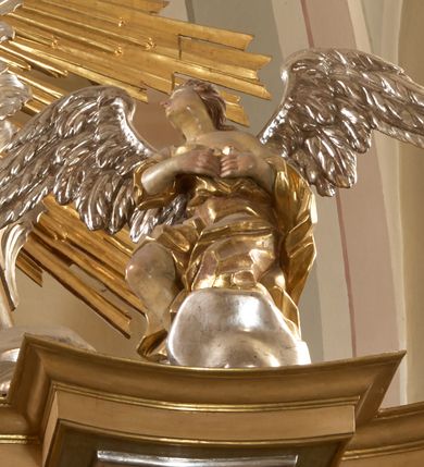 Zdjęcie nr 12: Ołtarz architektoniczny, jednokondygnacyjny, jednoosiowy, ze zwieńczeniem. Nastawa zbudowana na kamiennym, wysokim cokole, lekko wklęsła, ujęta zwielokrotnionymi pilastrami kompozytowymi o kanelowanych trzonach i zewnętrznymi, nieznacznie cofniętymi kolumnami, podtrzymującymi wyłamujące się nad nimi belkowanie. Po bokach karbowane taśmy z motywem liści akantu. W centrum obraz &quot;Przemienienie Pańskie&quot;. Nad pilastrami klęczące na obłokach uskrzydlone, adorujące anioły. Zwieńczenie o łukowato wygiętej podstawie i wklęsłych nieznacznie bokach, zwieńczone wyłamanym ku górze gzymsem zakończonym po bokach wolutami. W zwieńczenie wkomponowana okazała gloria promienista, z figurą Boga Ojca siedzącego w chmurach, Gołębicą Ducha Świętego i ukazaną na tle gzymsu postacią Archanioła Michała, ukazanego w zbroi, płaszczu na ramionach i w hełmie na głowie z mieczem w prawej dłoni. Na belkowaniu okazały kartusz ujęty puklowaną wstęgą i zwieńczony muszlą, z malowanym na srebrnym tle napisem: &quot;CHRISTO / TRANSFIGURATO / Hic est Filius meus dilectus / in quo mihi bene complacui / ipsum audite. / Matth: c. 77&quot;. Na ścianach prezbiterium, przed ołtarzem, na konsolach dwie figury św. Andrzej i św. Mateusz (?). Nastawa w całości złocona, partiami srebrzona (chmury, skrzydła aniołów, rama zwieńczenia, wstęga regencyjna po bokach), partie cokołu i fryzu z imitacją marmoryzacji.   

