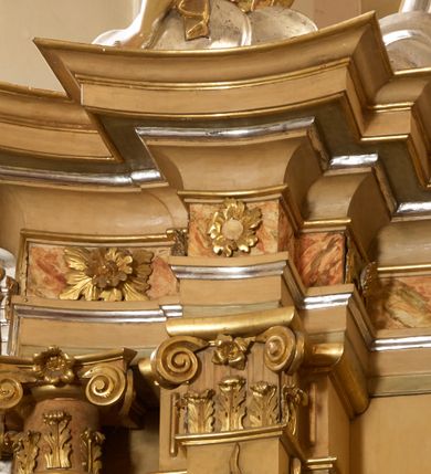 Zdjęcie nr 14: Ołtarz architektoniczny, jednokondygnacyjny, jednoosiowy, ze zwieńczeniem. Nastawa zbudowana na kamiennym, wysokim cokole, lekko wklęsła, ujęta zwielokrotnionymi pilastrami kompozytowymi o kanelowanych trzonach i zewnętrznymi, nieznacznie cofniętymi kolumnami, podtrzymującymi wyłamujące się nad nimi belkowanie. Po bokach karbowane taśmy z motywem liści akantu. W centrum obraz "Przemienienie Pańskie". Nad pilastrami klęczące na obłokach uskrzydlone, adorujące anioły. Zwieńczenie o łukowato wygiętej podstawie i wklęsłych nieznacznie bokach, zwieńczone wyłamanym ku górze gzymsem zakończonym po bokach wolutami. W zwieńczenie wkomponowana okazała gloria promienista, z figurą Boga Ojca siedzącego w chmurach, Gołębicą Ducha Świętego i ukazaną na tle gzymsu postacią Archanioła Michała, ukazanego w zbroi, płaszczu na ramionach i w hełmie na głowie z mieczem w prawej dłoni. Na belkowaniu okazały kartusz ujęty puklowaną wstęgą i zwieńczony muszlą, z malowanym na srebrnym tle napisem: "CHRISTO / TRANSFIGURATO / Hic est Filius meus dilectus / in quo mihi bene complacui / ipsum audite. / Matth: c. 77". Na ścianach prezbiterium, przed ołtarzem, na konsolach dwie figury św. Andrzej i św. Mateusz (?). Nastawa w całości złocona, partiami srebrzona (chmury, skrzydła aniołów, rama zwieńczenia, wstęga regencyjna po bokach), partie cokołu i fryzu z imitacją marmoryzacji.   

