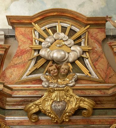 Zdjęcie nr 14: Retabulum architektoniczne, jednoosiowe, jednokondygnacyjne, ze zwieńczeniem,  posadowione na wysokim cokole. Nastawa ujęta ukośnie ustawionymi połówkami filarów na tle pilastrów, o kapitelach kompozytowych, podtrzymujących wydatne, przełamujące się nad nimi belkowanie z impostami i zwróconymi ku przodowi naczółkami, na których uskrzydlone, nagie putta, przepasane tkaninami. Zwieńczenie o lekko wklęsłych bokach zakończone gzymsem w formie łuku nadwieszonego. W partii fryzu kartusz ujęty wolutami, z lambrekinem u dołu, z muszlą palmetową u góry. W zwieńczeniu Oko Opatrzności na tle obłoków i promienistej glorii oraz dwie uskrzydlone główki anielskie. Dekorację ornamentalną tworzą kratki regencyjne, kampanule i muszle palmetowe. W części środkowej, we wnęce prostokątnej zamkniętej łukiem nadwieszonym półkolistym, w profilowanym obramieniu obraz Św. Katarzyna w profilowanej, prostokątnej ramie, nad nią rozłożysta palmeta. Wnęka ujęta kampanulami i gałązkami palmowymi. Po bokach nastawy dwie niezidentyfikowane postacie mężczyzn, całopostaciowe, w długich, silnie drapowanych sukniach, o wyrazistych twarzach, z krótkim zarostem i lekko falującymi włosami. Polichromia imitująca marmoryzację w odcieniach jasnych brązów, czerwieni i zieleni, figury o naturalnych karnacjach, złocenia szat figur i ornamentów, srebrzenia drobnych detali ornamentalnych.      
     
