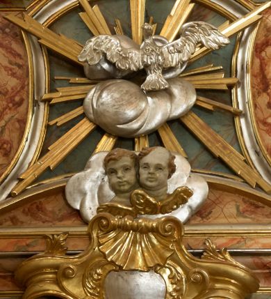 Zdjęcie nr 16: Retabulum architektoniczne, jednoosiowe, jednokondygnacyjne, ze zwieńczeniem, wzniesione na wysokim cokole. Nastawa ujęta ukośnie ustawionymi połówkami filarów na tle pilastrów, o kapitelach kompozytowych, podtrzymujących wydatne, przełamujące się nad nimi belkowanie z impostami i zwróconymi ku przodowi naczółkami, na których siedzą uskrzydlone, nagie putta, przepasane tkaninami. Zwieńczenie o lekko wklęsłych bokach zakończone gzymsem w formie łuku nadwieszonego. W partii fryzu kartusz ujęty wolutami, z lambrekinem u dołu z muszlą palmetową u góry. W zwieńczeniu gołębica Ducha Świętego na tle obłoków i promienistej glorii. Dekorację ornamentalną tworzą kratki regencyjne, kampanule i muszle palmetowe. W części środkowej obraz Matki Boskiej z Dzieciątkiem w typie Matki Boskiej Śnieżnej w drewnianej, złoconej sukience z koronami na głowie. Obraz z profilowanej ramie, złoconej i srebrzonej, ujętej po bokach zwisami z liści i kwiatów. Ponad obrazem rozłożysta muszla palmetowa. Po bokach nastawy dwie niezidentyfikowane postacie mężczyzn, całopostaciowe, w długich sukniach, z płaszczami zarzuconymi na ramiona, jedna z otwartą księgą w prawej dłoni, druga z rękoma złożonymi w geście modlitwy. Polichromia imitująca marmoryzację w odcieniach jasnych brązów, czerwieni i zieleni, figury o naturalnych karnacjach, złocenia szat figur i ornamentów, srebrzenia drobnych detali ornamentalnych.      


