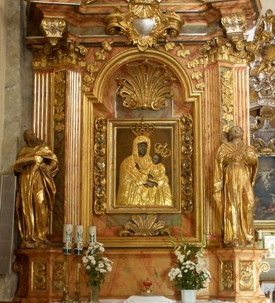 Zdjęcie nr 1: Retabulum architektoniczne, jednoosiowe, jednokondygnacyjne, ze zwieńczeniem, wzniesione na wysokim cokole. Nastawa ujęta ukośnie ustawionymi połówkami filarów na tle pilastrów, o kapitelach kompozytowych, podtrzymujących wydatne, przełamujące się nad nimi belkowanie z impostami i zwróconymi ku przodowi naczółkami, na których siedzą uskrzydlone, nagie putta, przepasane tkaninami. Zwieńczenie o lekko wklęsłych bokach zakończone gzymsem w formie łuku nadwieszonego. W partii fryzu kartusz ujęty wolutami, z lambrekinem u dołu z muszlą palmetową u góry. W zwieńczeniu gołębica Ducha Świętego na tle obłoków i promienistej glorii. Dekorację ornamentalną tworzą kratki regencyjne, kampanule i muszle palmetowe. W części środkowej obraz Matki Boskiej z Dzieciątkiem w typie Matki Boskiej Śnieżnej w drewnianej, złoconej sukience z koronami na głowie. Obraz z profilowanej ramie, złoconej i srebrzonej, ujętej po bokach zwisami z liści i kwiatów. Ponad obrazem rozłożysta muszla palmetowa. Po bokach nastawy dwie niezidentyfikowane postacie mężczyzn, całopostaciowe, w długich sukniach, z płaszczami zarzuconymi na ramiona, jedna z otwartą księgą w prawej dłoni, druga z rękoma złożonymi w geście modlitwy. Polichromia imitująca marmoryzację w odcieniach jasnych brązów, czerwieni i zieleni, figury o naturalnych karnacjach, złocenia szat figur i ornamentów, srebrzenia drobnych detali ornamentalnych.      


