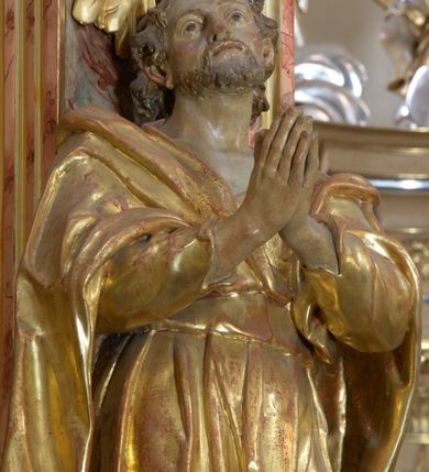 Zdjęcie nr 5: Retabulum architektoniczne, jednoosiowe, jednokondygnacyjne, ze zwieńczeniem, wzniesione na wysokim cokole. Nastawa ujęta ukośnie ustawionymi połówkami filarów na tle pilastrów, o kapitelach kompozytowych, podtrzymujących wydatne, przełamujące się nad nimi belkowanie z impostami i zwróconymi ku przodowi naczółkami, na których siedzą uskrzydlone, nagie putta, przepasane tkaninami. Zwieńczenie o lekko wklęsłych bokach zakończone gzymsem w formie łuku nadwieszonego. W partii fryzu kartusz ujęty wolutami, z lambrekinem u dołu z muszlą palmetową u góry. W zwieńczeniu gołębica Ducha Świętego na tle obłoków i promienistej glorii. Dekorację ornamentalną tworzą kratki regencyjne, kampanule i muszle palmetowe. W części środkowej obraz Matki Boskiej z Dzieciątkiem w typie Matki Boskiej Śnieżnej w drewnianej, złoconej sukience z koronami na głowie. Obraz z profilowanej ramie, złoconej i srebrzonej, ujętej po bokach zwisami z liści i kwiatów. Ponad obrazem rozłożysta muszla palmetowa. Po bokach nastawy dwie niezidentyfikowane postacie mężczyzn, całopostaciowe, w długich sukniach, z płaszczami zarzuconymi na ramiona, jedna z otwartą księgą w prawej dłoni, druga z rękoma złożonymi w geście modlitwy. Polichromia imitująca marmoryzację w odcieniach jasnych brązów, czerwieni i zieleni, figury o naturalnych karnacjach, złocenia szat figur i ornamentów, srebrzenia drobnych detali ornamentalnych.      


