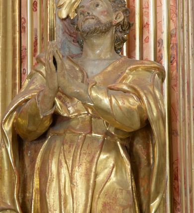 Zdjęcie nr 10: Retabulum architektoniczne, jednoosiowe, jednokondygnacyjne, ze zwieńczeniem, wzniesione na wysokim cokole. Nastawa ujęta ukośnie ustawionymi połówkami filarów na tle pilastrów, o kapitelach kompozytowych, podtrzymujących wydatne, przełamujące się nad nimi belkowanie z impostami i zwróconymi ku przodowi naczółkami, na których siedzą uskrzydlone, nagie putta, przepasane tkaninami. Zwieńczenie o lekko wklęsłych bokach zakończone gzymsem w formie łuku nadwieszonego. W partii fryzu kartusz ujęty wolutami, z lambrekinem u dołu z muszlą palmetową u góry. W zwieńczeniu gołębica Ducha Świętego na tle obłoków i promienistej glorii. Dekorację ornamentalną tworzą kratki regencyjne, kampanule i muszle palmetowe. W części środkowej obraz Matki Boskiej z Dzieciątkiem w typie Matki Boskiej Śnieżnej w drewnianej, złoconej sukience z koronami na głowie. Obraz z profilowanej ramie, złoconej i srebrzonej, ujętej po bokach zwisami z liści i kwiatów. Ponad obrazem rozłożysta muszla palmetowa. Po bokach nastawy dwie niezidentyfikowane postacie mężczyzn, całopostaciowe, w długich sukniach, z płaszczami zarzuconymi na ramiona, jedna z otwartą księgą w prawej dłoni, druga z rękoma złożonymi w geście modlitwy. Polichromia imitująca marmoryzację w odcieniach jasnych brązów, czerwieni i zieleni, figury o naturalnych karnacjach, złocenia szat figur i ornamentów, srebrzenia drobnych detali ornamentalnych.      


