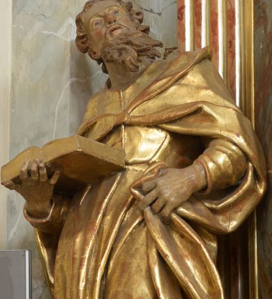 Zdjęcie nr 7: Retabulum architektoniczne, jednoosiowe, jednokondygnacyjne, ze zwieńczeniem, wzniesione na wysokim cokole. Nastawa ujęta ukośnie ustawionymi połówkami filarów na tle pilastrów, o kapitelach kompozytowych, podtrzymujących wydatne, przełamujące się nad nimi belkowanie z impostami i zwróconymi ku przodowi naczółkami, na których siedzą uskrzydlone, nagie putta, przepasane tkaninami. Zwieńczenie o lekko wklęsłych bokach zakończone gzymsem w formie łuku nadwieszonego. W partii fryzu kartusz ujęty wolutami, z lambrekinem u dołu z muszlą palmetową u góry. W zwieńczeniu gołębica Ducha Świętego na tle obłoków i promienistej glorii. Dekorację ornamentalną tworzą kratki regencyjne, kampanule i muszle palmetowe. W części środkowej obraz Matki Boskiej z Dzieciątkiem w typie Matki Boskiej Śnieżnej w drewnianej, złoconej sukience z koronami na głowie. Obraz z profilowanej ramie, złoconej i srebrzonej, ujętej po bokach zwisami z liści i kwiatów. Ponad obrazem rozłożysta muszla palmetowa. Po bokach nastawy dwie niezidentyfikowane postacie mężczyzn, całopostaciowe, w długich sukniach, z płaszczami zarzuconymi na ramiona, jedna z otwartą księgą w prawej dłoni, druga z rękoma złożonymi w geście modlitwy. Polichromia imitująca marmoryzację w odcieniach jasnych brązów, czerwieni i zieleni, figury o naturalnych karnacjach, złocenia szat figur i ornamentów, srebrzenia drobnych detali ornamentalnych.      


