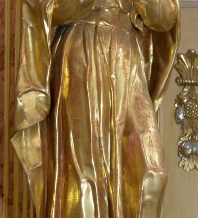 Zdjęcie nr 8: Retabulum architektoniczne, jednoosiowe, jednokondygnacyjne, ze zwieńczeniem, wzniesione na wysokim cokole. Nastawa ujęta ukośnie ustawionymi połówkami filarów na tle pilastrów, o kapitelach kompozytowych, podtrzymujących wydatne, przełamujące się nad nimi belkowanie z impostami i zwróconymi ku przodowi naczółkami, na których siedzą uskrzydlone, nagie putta, przepasane tkaninami. Zwieńczenie o lekko wklęsłych bokach zakończone gzymsem w formie łuku nadwieszonego. W partii fryzu kartusz ujęty wolutami, z lambrekinem u dołu z muszlą palmetową u góry. W zwieńczeniu gołębica Ducha Świętego na tle obłoków i promienistej glorii. Dekorację ornamentalną tworzą kratki regencyjne, kampanule i muszle palmetowe. W części środkowej obraz Matki Boskiej z Dzieciątkiem w typie Matki Boskiej Śnieżnej w drewnianej, złoconej sukience z koronami na głowie. Obraz z profilowanej ramie, złoconej i srebrzonej, ujętej po bokach zwisami z liści i kwiatów. Ponad obrazem rozłożysta muszla palmetowa. Po bokach nastawy dwie niezidentyfikowane postacie mężczyzn, całopostaciowe, w długich sukniach, z płaszczami zarzuconymi na ramiona, jedna z otwartą księgą w prawej dłoni, druga z rękoma złożonymi w geście modlitwy. Polichromia imitująca marmoryzację w odcieniach jasnych brązów, czerwieni i zieleni, figury o naturalnych karnacjach, złocenia szat figur i ornamentów, srebrzenia drobnych detali ornamentalnych.      


