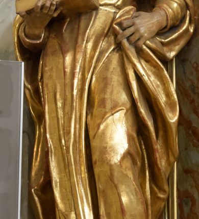 Zdjęcie nr 11: Retabulum architektoniczne, jednoosiowe, jednokondygnacyjne, ze zwieńczeniem, wzniesione na wysokim cokole. Nastawa ujęta ukośnie ustawionymi połówkami filarów na tle pilastrów, o kapitelach kompozytowych, podtrzymujących wydatne, przełamujące się nad nimi belkowanie z impostami i zwróconymi ku przodowi naczółkami, na których siedzą uskrzydlone, nagie putta, przepasane tkaninami. Zwieńczenie o lekko wklęsłych bokach zakończone gzymsem w formie łuku nadwieszonego. W partii fryzu kartusz ujęty wolutami, z lambrekinem u dołu z muszlą palmetową u góry. W zwieńczeniu gołębica Ducha Świętego na tle obłoków i promienistej glorii. Dekorację ornamentalną tworzą kratki regencyjne, kampanule i muszle palmetowe. W części środkowej obraz Matki Boskiej z Dzieciątkiem w typie Matki Boskiej Śnieżnej w drewnianej, złoconej sukience z koronami na głowie. Obraz z profilowanej ramie, złoconej i srebrzonej, ujętej po bokach zwisami z liści i kwiatów. Ponad obrazem rozłożysta muszla palmetowa. Po bokach nastawy dwie niezidentyfikowane postacie mężczyzn, całopostaciowe, w długich sukniach, z płaszczami zarzuconymi na ramiona, jedna z otwartą księgą w prawej dłoni, druga z rękoma złożonymi w geście modlitwy. Polichromia imitująca marmoryzację w odcieniach jasnych brązów, czerwieni i zieleni, figury o naturalnych karnacjach, złocenia szat figur i ornamentów, srebrzenia drobnych detali ornamentalnych.      


