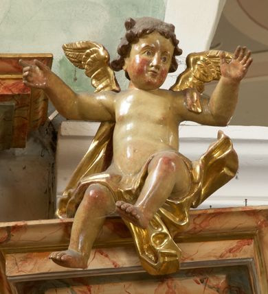 Zdjęcie nr 18: Retabulum architektoniczne, jednoosiowe, jednokondygnacyjne, ze zwieńczeniem, wzniesione na wysokim cokole. Nastawa ujęta ukośnie ustawionymi połówkami filarów na tle pilastrów, o kapitelach kompozytowych, podtrzymujących wydatne, przełamujące się nad nimi belkowanie z impostami i zwróconymi ku przodowi naczółkami, na których siedzą uskrzydlone, nagie putta, przepasane tkaninami. Zwieńczenie o lekko wklęsłych bokach zakończone gzymsem w formie łuku nadwieszonego. W partii fryzu kartusz ujęty wolutami, z lambrekinem u dołu z muszlą palmetową u góry. W zwieńczeniu gołębica Ducha Świętego na tle obłoków i promienistej glorii. Dekorację ornamentalną tworzą kratki regencyjne, kampanule i muszle palmetowe. W części środkowej obraz Matki Boskiej z Dzieciątkiem w typie Matki Boskiej Śnieżnej w drewnianej, złoconej sukience z koronami na głowie. Obraz z profilowanej ramie, złoconej i srebrzonej, ujętej po bokach zwisami z liści i kwiatów. Ponad obrazem rozłożysta muszla palmetowa. Po bokach nastawy dwie niezidentyfikowane postacie mężczyzn, całopostaciowe, w długich sukniach, z płaszczami zarzuconymi na ramiona, jedna z otwartą księgą w prawej dłoni, druga z rękoma złożonymi w geście modlitwy. Polichromia imitująca marmoryzację w odcieniach jasnych brązów, czerwieni i zieleni, figury o naturalnych karnacjach, złocenia szat figur i ornamentów, srebrzenia drobnych detali ornamentalnych.      


