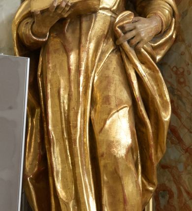 Zdjęcie nr 13: Retabulum architektoniczne, jednoosiowe, jednokondygnacyjne, ze zwieńczeniem, wzniesione na wysokim cokole. Nastawa ujęta ukośnie ustawionymi połówkami filarów na tle pilastrów, o kapitelach kompozytowych, podtrzymujących wydatne, przełamujące się nad nimi belkowanie z impostami i zwróconymi ku przodowi naczółkami, na których siedzą uskrzydlone, nagie putta, przepasane tkaninami. Zwieńczenie o lekko wklęsłych bokach zakończone gzymsem w formie łuku nadwieszonego. W partii fryzu kartusz ujęty wolutami, z lambrekinem u dołu z muszlą palmetową u góry. W zwieńczeniu gołębica Ducha Świętego na tle obłoków i promienistej glorii. Dekorację ornamentalną tworzą kratki regencyjne, kampanule i muszle palmetowe. W części środkowej obraz Matki Boskiej z Dzieciątkiem w typie Matki Boskiej Śnieżnej w drewnianej, złoconej sukience z koronami na głowie. Obraz z profilowanej ramie, złoconej i srebrzonej, ujętej po bokach zwisami z liści i kwiatów. Ponad obrazem rozłożysta muszla palmetowa. Po bokach nastawy dwie niezidentyfikowane postacie mężczyzn, całopostaciowe, w długich sukniach, z płaszczami zarzuconymi na ramiona, jedna z otwartą księgą w prawej dłoni, druga z rękoma złożonymi w geście modlitwy. Polichromia imitująca marmoryzację w odcieniach jasnych brązów, czerwieni i zieleni, figury o naturalnych karnacjach, złocenia szat figur i ornamentów, srebrzenia drobnych detali ornamentalnych.      


