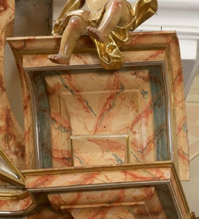 Zdjęcie nr 20: Retabulum architektoniczne, jednoosiowe, jednokondygnacyjne, ze zwieńczeniem, wzniesione na wysokim cokole. Nastawa ujęta ukośnie ustawionymi połówkami filarów na tle pilastrów, o kapitelach kompozytowych, podtrzymujących wydatne, przełamujące się nad nimi belkowanie z impostami i zwróconymi ku przodowi naczółkami, na których siedzą uskrzydlone, nagie putta, przepasane tkaninami. Zwieńczenie o lekko wklęsłych bokach zakończone gzymsem w formie łuku nadwieszonego. W partii fryzu kartusz ujęty wolutami, z lambrekinem u dołu z muszlą palmetową u góry. W zwieńczeniu gołębica Ducha Świętego na tle obłoków i promienistej glorii. Dekorację ornamentalną tworzą kratki regencyjne, kampanule i muszle palmetowe. W części środkowej obraz Matki Boskiej z Dzieciątkiem w typie Matki Boskiej Śnieżnej w drewnianej, złoconej sukience z koronami na głowie. Obraz z profilowanej ramie, złoconej i srebrzonej, ujętej po bokach zwisami z liści i kwiatów. Ponad obrazem rozłożysta muszla palmetowa. Po bokach nastawy dwie niezidentyfikowane postacie mężczyzn, całopostaciowe, w długich sukniach, z płaszczami zarzuconymi na ramiona, jedna z otwartą księgą w prawej dłoni, druga z rękoma złożonymi w geście modlitwy. Polichromia imitująca marmoryzację w odcieniach jasnych brązów, czerwieni i zieleni, figury o naturalnych karnacjach, złocenia szat figur i ornamentów, srebrzenia drobnych detali ornamentalnych.      


