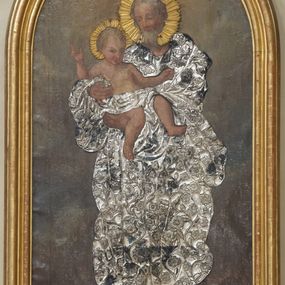 Zdjęcie nr 1: Obraz w kształcie stojącego prostokąta zamkniętego półkoliście w drewnianej, profilowanej, złoconej ramie. W centrum przedstawienia znajduje się stojący frontalnie w lekkim kontrapoście św. Józef trzymający oburącz Dzieciątko Jezus. Święty spogląda czule na Jezusa, ma owalną, łagodną twarz, migdałowe, półprzymknięte oczy, wąski nos, małe usta oraz delikatne rumieńce. Dzieciątko patrzy na widza, lewą rękę wyciąga do boku, prawą unosi w geście błogosławieństwa, zgięte w kolanach nogi ma luźno opuszczone. Na okrągłej twarzy wyróżniają się bystre, ciemne oczy, mały nos, wąskie usta oraz rumieńce. Święty Józef przyodziany jest w nałożoną na obraz metalową, długą, pofałdowaną, suknię pokrytą ornamentem roślinno-kwiatowym, która przechodzi w przepaskę na biodrach Jezusa. Głowy postaci otaczają aplikowane, złocone nimby promieniste. Scena rozgrywa się na ciemnym, rozjaśnionym wokół głów postaci tle.