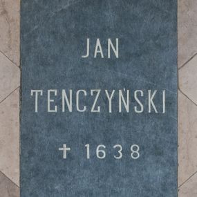 Zdjęcie nr 1: Płyta w kształcie stojącego prostokąta wykonana z ciemnego kamienia, wmurowana w posadzkę nawy głównej kościoła. Na niej kuty, podkreślony jasnym kolorem napis „JAN / TENCZYŃSKI / †1638” 