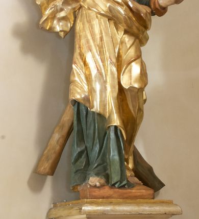 Zdjęcie nr 3: Święty został ukazany całopostaciowo, frontalnie, w kontrapoście, prawą ręką obejmuje belkę swojego krzyża. Jest ubrany w zieloną suknię sięgającą stóp i złoty płaszcz przerzucony przez prawe ramię i osłaniający do kolan korpus świętego. Głowę ma wzniesioną ku górze, okoloną długą, falującą brodą, z wydatnymi zakolami, otwartymi oczami i ustami. 