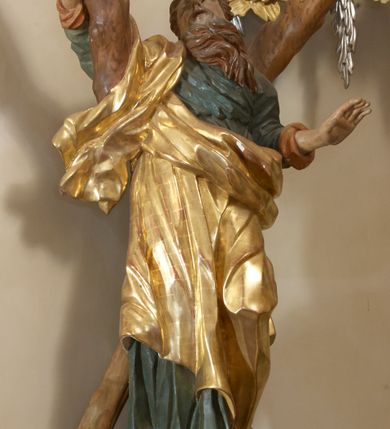 Zdjęcie nr 2: Święty został ukazany całopostaciowo, frontalnie, w kontrapoście, prawą ręką obejmuje belkę swojego krzyża. Jest ubrany w zieloną suknię sięgającą stóp i złoty płaszcz przerzucony przez prawe ramię i osłaniający do kolan korpus świętego. Głowę ma wzniesioną ku górze, okoloną długą, falującą brodą, z wydatnymi zakolami, otwartymi oczami i ustami. 