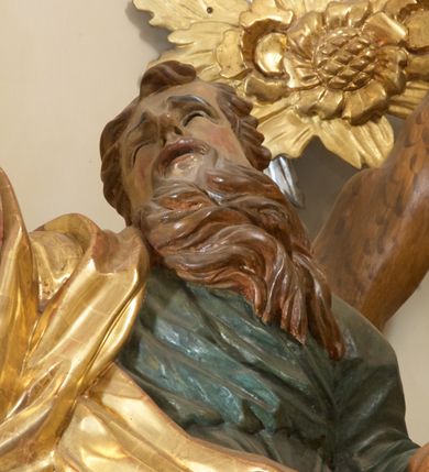 Zdjęcie nr 5: Święty został ukazany całopostaciowo, frontalnie, w kontrapoście, prawą ręką obejmuje belkę swojego krzyża. Jest ubrany w zieloną suknię sięgającą stóp i złoty płaszcz przerzucony przez prawe ramię i osłaniający do kolan korpus świętego. Głowę ma wzniesioną ku górze, okoloną długą, falującą brodą, z wydatnymi zakolami, otwartymi oczami i ustami. 