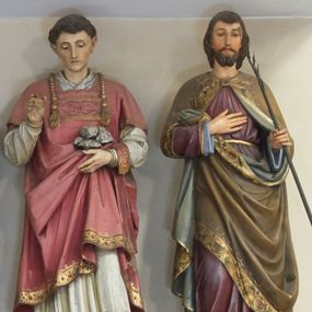 Zdjęcie nr 1: Figura pełna na cokole przedstawiająca św. Walentego. Święty stoi frontalnie, spoglądając przed siebie. Ma trójkątną twarz, małe oczy, wąski nos, niewielkie usta i krótkie, ciemne włosy. Prawą rękę wyciąga przed siebie w delikatnym geście, lewą przytrzymuje zamkniętą księgę. Ubrany jest w białą komżę zdobioną przy rękawach i dolnej krawędzi szerokim pasem koronki oraz złoty ornat dekorowany motywami winnej latorośli z monogramami Chrystusa na kolumnie – pionowym pasie biegnącym przez środek szaty. Spod ornatu wystają końce złotej stuły zakończonej krzyżami równoramiennymi i frędzlami, przez lewe przedramię przewieszony ma manipularz. 
Na cokole napis „S(anc)t(us) Valentinus”.
