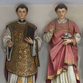 Zdjęcie nr 1: Figura pełna na cokole przedstawiająca św. Szczepana. Święty stoi frontalnie, kierując wzrok w dół. Ma trójkątną twarz, małe oczy, wąski nos i niewielkie usta oraz ciemne, krótki włosy. Prawą rękę, w której brakuje atrybutu (być może gałązki palmowej) unosi przed siebie, lewą przytrzymuje fałdy szaty, w której niesie niewielki stos kamieni. Ubrany jest w białą rokietę zdobioną przy dolnej krawędzi szerokim pasem koronki oraz czerwoną dalmatykę dekorowaną pod szyją i lamowaną złotą taśmą zdobioną przy dolnej krawędzi drogimi kamieniami. Przez lewe przedramię ma przewieszony manipularz. 
Na cokole napis „S[anctus] [Step]han[us]”.