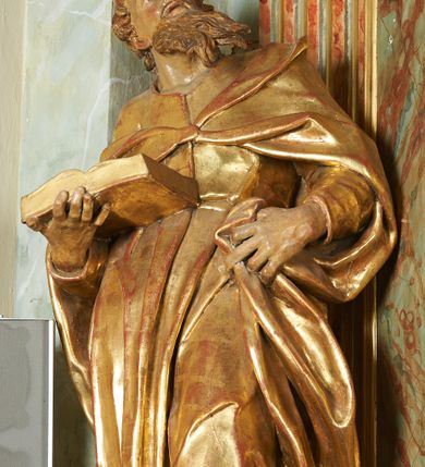 Zdjęcie nr 4: Figura ukazuje mężczyznę w całej postaci, w kontrapoście, ubranego w długą suknię przewiązaną w pasie i płaszcz spięty na piersiach, z otwartą księgą na prawej dłoni, z lewą przytrzymującą na biodrach płaszcz. Głowa zwrócona w lewo, ku górze, okolona długą, falującą brodą. 