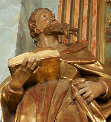 Zdjęcie nr 6: Figura ukazuje mężczyznę w całej postaci, w kontrapoście, ubranego w długą suknię przewiązaną w pasie i płaszcz spięty na piersiach, z otwartą księgą na prawej dłoni, z lewą przytrzymującą na biodrach płaszcz. Głowa zwrócona w lewo, ku górze, okolona długą, falującą brodą. 