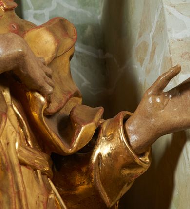 Zdjęcie nr 6: Rzeźba z ołtarza św. Katarzyny przedstawia świętego stojącego w lekkim wykroku z lewą nogą nieco wysuniętą do przodu. Głowa lekko pochylona, włosy kręcone, broda długa. Prawą rękę trzyma na piersi, lewa jest ugięta i uniesiona. Płaszcz i tunika bogato drapowane i złocone.