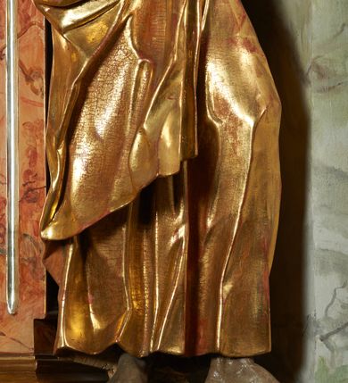 Zdjęcie nr 7: Rzeźba z ołtarza św. Katarzyny przedstawia świętego stojącego w lekkim wykroku z lewą nogą nieco wysuniętą do przodu. Głowa lekko pochylona, włosy kręcone, broda długa. Prawą rękę trzyma na piersi, lewa jest ugięta i uniesiona. Płaszcz i tunika bogato drapowane i złocone.