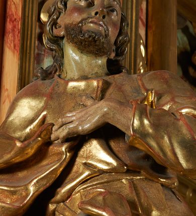 Zdjęcie nr 5: Rzeźba z ołtarza św. Katarzyny przedstawia świętego w lekkim wykroku z prawą nogą nieco wysuniętą do przodu. Wzrok zwrócony przed siebie, włosy długie, broda krótka. Lewa ręka jest położona na piersi, zaś prawa opuszczona i lekko odsunięta od ciała. Płaszcz i tunika bogato drapowane i złocone.