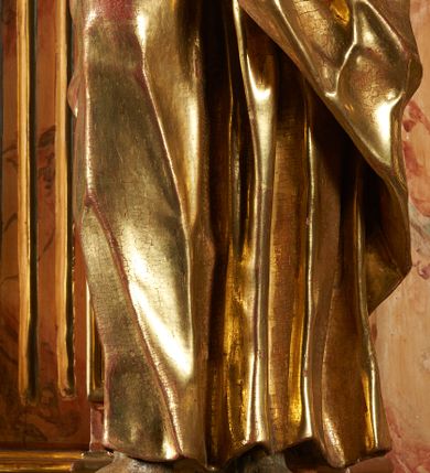 Zdjęcie nr 7: Rzeźba z ołtarza św. Katarzyny przedstawia świętego w lekkim wykroku z prawą nogą nieco wysuniętą do przodu. Wzrok zwrócony przed siebie, włosy długie, broda krótka. Lewa ręka jest położona na piersi, zaś prawa opuszczona i lekko odsunięta od ciała. Płaszcz i tunika bogato drapowane i złocone.