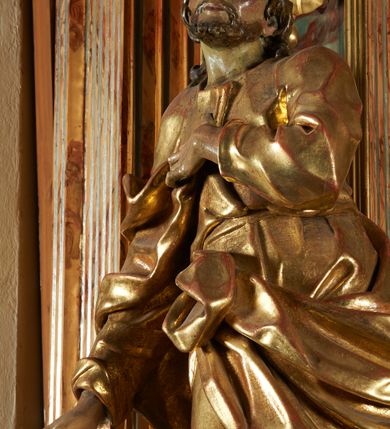 Zdjęcie nr 6: Rzeźba z ołtarza św. Katarzyny przedstawia świętego w lekkim wykroku z prawą nogą nieco wysuniętą do przodu. Wzrok zwrócony przed siebie, włosy długie, broda krótka. Lewa ręka jest położona na piersi, zaś prawa opuszczona i lekko odsunięta od ciała. Płaszcz i tunika bogato drapowane i złocone.