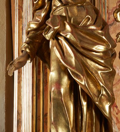 Zdjęcie nr 4: Rzeźba z ołtarza św. Katarzyny przedstawia świętego w lekkim wykroku z prawą nogą nieco wysuniętą do przodu. Wzrok zwrócony przed siebie, włosy długie, broda krótka. Lewa ręka jest położona na piersi, zaś prawa opuszczona i lekko odsunięta od ciała. Płaszcz i tunika bogato drapowane i złocone.