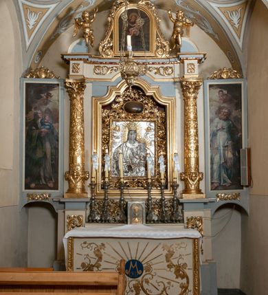 Zdjęcie nr 2: Ołtarz przyścienny, architektoniczny, jednokondygnacyjny ze zwieńczeniem, trójosiowy z bramkami. Mensa murowana prostopadłościenna, antepedium drewniane w złoconej ramie dekorowanej akantem. W jego polu medalion z monogramem maryjnym w glorii promienistej, otoczony przestylizowaną winoroślą. Tabernakulum w osi, metalowe, prostopadłościenne, jednodrzwiczkowe, z przedstawieniem kielicha z hostią. Retabulum ołtarzowe drewniane na cokole. Pole ołtarza z prostokątną, profilowaną ramą zamkniętą łukiem wklęsło-wypukłym z uskokiem. Mieści obraz Matki Boskiej Szkaplerznej, w bogatej akantowo-kwiatowej ramie z umieszczonym u góry, w osi owalnym obrazem Boga Ojca; zasuwany obrazami św. Józefa oraz św. Izydora Oracza. Pole jest ujęte ustawionymi na wysokich cokołach dekorowanych akantem, kolumnami o trzonach wypełnionych ornamentem roślinno-kwiatowym o układzie kandelabrowym oraz u podstawy z pełnoplastycznymi, uskrzydlonymi główkami aniołów; kapitele kompozytowe. Kolumny dźwigają niepełne, wyniesione pośrodku belkowanie, z odcinkami półkolistego przyczółka, na którym siedzą pełnoplastyczne, złocone figurki puttów. Fryz dekorowany akantem. W zwieńczeniu obraz św. Antoniego Padewskiego, prostokątny, zamknięty półkoliście, ujęty akantowymi wolutami. W bocznych osiach, ponad bramkami, prostokątne obrazy z lewej: św. Anny, z prawej: św. Joachima, dekorowane złoconym, ażurowym zwieńczeniem z kartuszy ujętych akantem. Ołtarz utrzymany w odcieniach beżu i szarości ze złoceniami w partiach ornamentów oraz w załamaniach profili architektonicznych.
