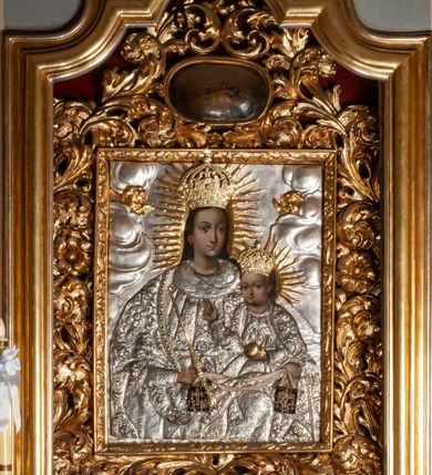 Zdjęcie nr 3: Ołtarz przyścienny, architektoniczny, jednokondygnacyjny ze zwieńczeniem, trójosiowy z bramkami. Mensa murowana prostopadłościenna, antepedium drewniane w złoconej ramie dekorowanej akantem. W jego polu medalion z monogramem maryjnym w glorii promienistej, otoczony przestylizowaną winoroślą. Tabernakulum w osi, metalowe, prostopadłościenne, jednodrzwiczkowe, z przedstawieniem kielicha z hostią. Retabulum ołtarzowe drewniane na cokole. Pole ołtarza z prostokątną, profilowaną ramą zamkniętą łukiem wklęsło-wypukłym z uskokiem. Mieści obraz Matki Boskiej Szkaplerznej, w bogatej akantowo-kwiatowej ramie z umieszczonym u góry, w osi owalnym obrazem Boga Ojca; zasuwany obrazami św. Józefa oraz św. Izydora Oracza. Pole jest ujęte ustawionymi na wysokich cokołach dekorowanych akantem, kolumnami o trzonach wypełnionych ornamentem roślinno-kwiatowym o układzie kandelabrowym oraz u podstawy z pełnoplastycznymi, uskrzydlonymi główkami aniołów; kapitele kompozytowe. Kolumny dźwigają niepełne, wyniesione pośrodku belkowanie, z odcinkami półkolistego przyczółka, na którym siedzą pełnoplastyczne, złocone figurki puttów. Fryz dekorowany akantem. W zwieńczeniu obraz św. Antoniego Padewskiego, prostokątny, zamknięty półkoliście, ujęty akantowymi wolutami. W bocznych osiach, ponad bramkami, prostokątne obrazy z lewej: św. Anny, z prawej: św. Joachima, dekorowane złoconym, ażurowym zwieńczeniem z kartuszy ujętych akantem. Ołtarz utrzymany w odcieniach beżu i szarości ze złoceniami w partiach ornamentów oraz w załamaniach profili architektonicznych.