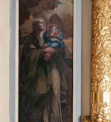 Zdjęcie nr 48: Ołtarz przyścienny, architektoniczny, jednokondygnacyjny ze zwieńczeniem, trójosiowy z bramkami. Mensa murowana prostopadłościenna, antepedium drewniane w złoconej ramie dekorowanej akantem. W jego polu medalion z monogramem maryjnym w glorii promienistej, otoczony przestylizowaną winoroślą. Tabernakulum w osi, metalowe, prostopadłościenne, jednodrzwiczkowe, z przedstawieniem kielicha z hostią. Retabulum ołtarzowe drewniane na cokole. Pole ołtarza z prostokątną, profilowaną ramą zamkniętą łukiem wklęsło-wypukłym z uskokiem. Mieści obraz Matki Boskiej Szkaplerznej, w bogatej akantowo-kwiatowej ramie z umieszczonym u góry, w osi owalnym obrazem Boga Ojca; zasuwany obrazami św. Józefa oraz św. Izydora Oracza. Pole jest ujęte ustawionymi na wysokich cokołach dekorowanych akantem, kolumnami o trzonach wypełnionych ornamentem roślinno-kwiatowym o układzie kandelabrowym oraz u podstawy z pełnoplastycznymi, uskrzydlonymi główkami aniołów; kapitele kompozytowe. Kolumny dźwigają niepełne, wyniesione pośrodku belkowanie, z odcinkami półkolistego przyczółka, na którym siedzą pełnoplastyczne, złocone figurki puttów. Fryz dekorowany akantem. W zwieńczeniu obraz św. Antoniego Padewskiego, prostokątny, zamknięty półkoliście, ujęty akantowymi wolutami. W bocznych osiach, ponad bramkami, prostokątne obrazy z lewej: św. Anny, z prawej: św. Joachima, dekorowane złoconym, ażurowym zwieńczeniem z kartuszy ujętych akantem. Ołtarz utrzymany w odcieniach beżu i szarości ze złoceniami w partiach ornamentów oraz w załamaniach profili architektonicznych.