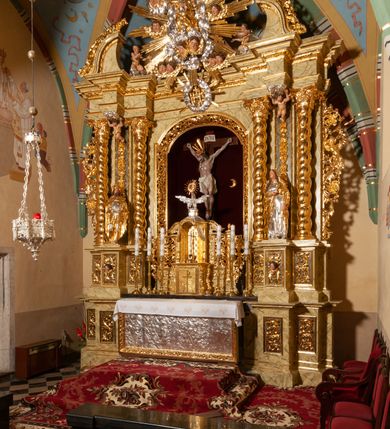 Zdjęcie nr 59: Drewniany, przyścienny ołtarz o formach architektonicznych, jednoosiowy, jednokondygnacyjny ze zwieńczeniem. Mensa murowana w kształcie prostopadłościanu zwieńczonego profilowanym gzymsem; antepedium prostokątne, w drewnianej, płaskorzeźbionej w motywy akantowe, złoconej ramie, dwustronne. Awers tłoczony, srebrzony, wykonany w technice papier mâché; rewers z malowanym na desce wyobrażeniem Veraicon na tle narzędzi męki. Tabernakulum na osi, złożone z mosiężnej, złoconej, sześciobocznej skrzynki w rozbudowanej, drewnianej obudowie o formach architektonicznych. Na nim tron wystawienia w kształcie niszy dekorowanej kratką, nakrytej kopułką z latarnią i przysłoniętej złapanymi po bokach kotarami. Na latarni rzeźbione przedstawienie pelikana karmiącego pisklęta własną krwią. Skrzynkę z tronem ulokowano na tle parawanu ustawionego na podwójnym cokole, ażurowego w górnej części, wypełnionego dekoracją roślinną, złączonego z kopułka spływami. 
Retabulum ołtarzowe drewniane wsparte na wysokim, dwudzielnym, murowanym cokole. Cokół w obudowie drewnianej, jego kondygnacje wydzielone wydatnymi, silnie występującymi przed lico gzymsami; mocno wysunięte ku przodowi części przednie. Ich lica z prostokątnymi płycinami mieszczącymi suchy akant; w części środkowej drugiej kondygnacji cokołu, dodatkowo pełnoplastyczne główki puttów. Na cokole ustawione zdwojone, złocone kolumny o skręconych trzonach i kompozytowych kapitelach. Pomiędzy nimi płyciny wypełnione dekoracją w formie podwieszonego wieńca, u jego szczytu putta pełniące rolę atlantów. Na tle płycin ustawione drewniane, złocone figury z lewej św. Zygmunta i z prawej św. Marii Magdaleny – patronów kościoła. Pole ołtarza z prostokątną niszą zamkniętą łukiem wyniesionym; ujętą płaskorzeźbioną, złoconą ramą zdobioną suchym akantem. W niszy pełnoplastyczny, polichromowany i złocony krucyfiks na aksamitnym tle, flankowany przez płaskorzeźbione wyobrażenia słońca i księżyca. Nisza zasuwana obrazem z Przemienieniem na górze Tabor, w drewnianej, złoconej sukience. Kolumny dźwigają pełne, wyłamane na osiach podpór belkowanie, z wydatnym, silnie profilowanym gzymsem; na jego osi złocony monogram „IHS” w otoku ze srebrzonych obłoków na tle promienistej glorii. Całość wieńczą fragmenty przerwanego przyczółka o formach wklęsło-wypukłych, z ażurową dekoracją z suchego akantu. Pomiędzy ramionami przyczółka złocona gloria promienista, w centrum której płaskorzeźbiona postać Boga Ojca siedzącego na srebrzonym obłoku ze srebrzoną gołębicą Ducha Świętego u stóp. Na ramionach glorii uskrzydlone główki puttów, niektóre na tle obłoków. Po bokach, na gzymsie siedzące postaci nagich, adorujących puttów. Ołtarz ujęty ażurowymi, złoconymi uszami z suchego akantu, w który wplecione są groteskowe putta trzymające pochodnie. Większość powierzchni ołtarza marmoryzowana, w kolorze jasnej, oliwkowej zieleni, z ciemniejszymi brązowymi elementami wypełniającymi płyciny. Złocenia w partiach ornamentów, kolumn oraz załamaniach profili elementów architektonicznych; srebrzone obłoki, części szat postaci i pelikan. 