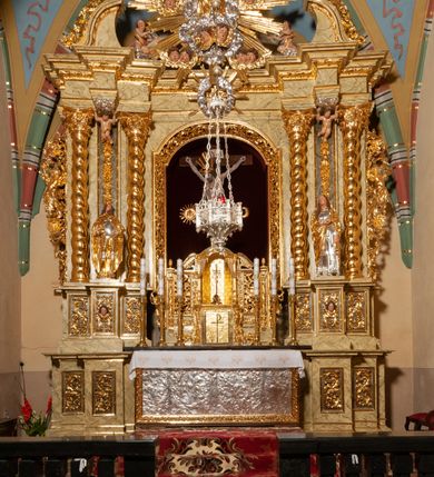 Zdjęcie nr 60: Drewniany, przyścienny ołtarz o formach architektonicznych, jednoosiowy, jednokondygnacyjny ze zwieńczeniem. Mensa murowana w kształcie prostopadłościanu zwieńczonego profilowanym gzymsem; antepedium prostokątne, w drewnianej, płaskorzeźbionej w motywy akantowe, złoconej ramie, dwustronne. Awers tłoczony, srebrzony, wykonany w technice papier mâché; rewers z malowanym na desce wyobrażeniem Veraicon na tle narzędzi męki. Tabernakulum na osi, złożone z mosiężnej, złoconej, sześciobocznej skrzynki w rozbudowanej, drewnianej obudowie o formach architektonicznych. Na nim tron wystawienia w kształcie niszy dekorowanej kratką, nakrytej kopułką z latarnią i przysłoniętej złapanymi po bokach kotarami. Na latarni rzeźbione przedstawienie pelikana karmiącego pisklęta własną krwią. Skrzynkę z tronem ulokowano na tle parawanu ustawionego na podwójnym cokole, ażurowego w górnej części, wypełnionego dekoracją roślinną, złączonego z kopułka spływami. 
Retabulum ołtarzowe drewniane wsparte na wysokim, dwudzielnym, murowanym cokole. Cokół w obudowie drewnianej, jego kondygnacje wydzielone wydatnymi, silnie występującymi przed lico gzymsami; mocno wysunięte ku przodowi części przednie. Ich lica z prostokątnymi płycinami mieszczącymi suchy akant; w części środkowej drugiej kondygnacji cokołu, dodatkowo pełnoplastyczne główki puttów. Na cokole ustawione zdwojone, złocone kolumny o skręconych trzonach i kompozytowych kapitelach. Pomiędzy nimi płyciny wypełnione dekoracją w formie podwieszonego wieńca, u jego szczytu putta pełniące rolę atlantów. Na tle płycin ustawione drewniane, złocone figury z lewej św. Zygmunta i z prawej św. Marii Magdaleny – patronów kościoła. Pole ołtarza z prostokątną niszą zamkniętą łukiem wyniesionym; ujętą płaskorzeźbioną, złoconą ramą zdobioną suchym akantem. W niszy pełnoplastyczny, polichromowany i złocony krucyfiks na aksamitnym tle, flankowany przez płaskorzeźbione wyobrażenia słońca i księżyca. Nisza zasuwana obrazem z Przemienieniem na górze Tabor, w drewnianej, złoconej sukience. Kolumny dźwigają pełne, wyłamane na osiach podpór belkowanie, z wydatnym, silnie profilowanym gzymsem; na jego osi złocony monogram „IHS” w otoku ze srebrzonych obłoków na tle promienistej glorii. Całość wieńczą fragmenty przerwanego przyczółka o formach wklęsło-wypukłych, z ażurową dekoracją z suchego akantu. Pomiędzy ramionami przyczółka złocona gloria promienista, w centrum której płaskorzeźbiona postać Boga Ojca siedzącego na srebrzonym obłoku ze srebrzoną gołębicą Ducha Świętego u stóp. Na ramionach glorii uskrzydlone główki puttów, niektóre na tle obłoków. Po bokach, na gzymsie siedzące postaci nagich, adorujących puttów. Ołtarz ujęty ażurowymi, złoconymi uszami z suchego akantu, w który wplecione są groteskowe putta trzymające pochodnie. Większość powierzchni ołtarza marmoryzowana, w kolorze jasnej, oliwkowej zieleni, z ciemniejszymi brązowymi elementami wypełniającymi płyciny. Złocenia w partiach ornamentów, kolumn oraz załamaniach profili elementów architektonicznych; srebrzone obłoki, części szat postaci i pelikan. 