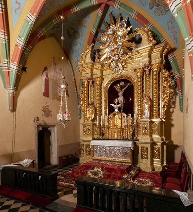 Zdjęcie nr 61: Drewniany, przyścienny ołtarz o formach architektonicznych, jednoosiowy, jednokondygnacyjny ze zwieńczeniem. Mensa murowana w kształcie prostopadłościanu zwieńczonego profilowanym gzymsem; antepedium prostokątne, w drewnianej, płaskorzeźbionej w motywy akantowe, złoconej ramie, dwustronne. Awers tłoczony, srebrzony, wykonany w technice papier mâché; rewers z malowanym na desce wyobrażeniem Veraicon na tle narzędzi męki. Tabernakulum na osi, złożone z mosiężnej, złoconej, sześciobocznej skrzynki w rozbudowanej, drewnianej obudowie o formach architektonicznych. Na nim tron wystawienia w kształcie niszy dekorowanej kratką, nakrytej kopułką z latarnią i przysłoniętej złapanymi po bokach kotarami. Na latarni rzeźbione przedstawienie pelikana karmiącego pisklęta własną krwią. Skrzynkę z tronem ulokowano na tle parawanu ustawionego na podwójnym cokole, ażurowego w górnej części, wypełnionego dekoracją roślinną, złączonego z kopułka spływami. 
Retabulum ołtarzowe drewniane wsparte na wysokim, dwudzielnym, murowanym cokole. Cokół w obudowie drewnianej, jego kondygnacje wydzielone wydatnymi, silnie występującymi przed lico gzymsami; mocno wysunięte ku przodowi części przednie. Ich lica z prostokątnymi płycinami mieszczącymi suchy akant; w części środkowej drugiej kondygnacji cokołu, dodatkowo pełnoplastyczne główki puttów. Na cokole ustawione zdwojone, złocone kolumny o skręconych trzonach i kompozytowych kapitelach. Pomiędzy nimi płyciny wypełnione dekoracją w formie podwieszonego wieńca, u jego szczytu putta pełniące rolę atlantów. Na tle płycin ustawione drewniane, złocone figury z lewej św. Zygmunta i z prawej św. Marii Magdaleny – patronów kościoła. Pole ołtarza z prostokątną niszą zamkniętą łukiem wyniesionym; ujętą płaskorzeźbioną, złoconą ramą zdobioną suchym akantem. W niszy pełnoplastyczny, polichromowany i złocony krucyfiks na aksamitnym tle, flankowany przez płaskorzeźbione wyobrażenia słońca i księżyca. Nisza zasuwana obrazem z Przemienieniem na górze Tabor, w drewnianej, złoconej sukience. Kolumny dźwigają pełne, wyłamane na osiach podpór belkowanie, z wydatnym, silnie profilowanym gzymsem; na jego osi złocony monogram „IHS” w otoku ze srebrzonych obłoków na tle promienistej glorii. Całość wieńczą fragmenty przerwanego przyczółka o formach wklęsło-wypukłych, z ażurową dekoracją z suchego akantu. Pomiędzy ramionami przyczółka złocona gloria promienista, w centrum której płaskorzeźbiona postać Boga Ojca siedzącego na srebrzonym obłoku ze srebrzoną gołębicą Ducha Świętego u stóp. Na ramionach glorii uskrzydlone główki puttów, niektóre na tle obłoków. Po bokach, na gzymsie siedzące postaci nagich, adorujących puttów. Ołtarz ujęty ażurowymi, złoconymi uszami z suchego akantu, w który wplecione są groteskowe putta trzymające pochodnie. Większość powierzchni ołtarza marmoryzowana, w kolorze jasnej, oliwkowej zieleni, z ciemniejszymi brązowymi elementami wypełniającymi płyciny. Złocenia w partiach ornamentów, kolumn oraz załamaniach profili elementów architektonicznych; srebrzone obłoki, części szat postaci i pelikan. 