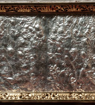 Zdjęcie nr 50: Drewniany, przyścienny ołtarz o formach architektonicznych, jednoosiowy, jednokondygnacyjny ze zwieńczeniem. Mensa murowana w kształcie prostopadłościanu zwieńczonego profilowanym gzymsem; antepedium prostokątne, w drewnianej, płaskorzeźbionej w motywy akantowe, złoconej ramie, dwustronne. Awers tłoczony, srebrzony, wykonany w technice papier mâché; rewers z malowanym na desce wyobrażeniem Veraicon na tle narzędzi męki. Tabernakulum na osi, złożone z mosiężnej, złoconej, sześciobocznej skrzynki w rozbudowanej, drewnianej obudowie o formach architektonicznych. Na nim tron wystawienia w kształcie niszy dekorowanej kratką, nakrytej kopułką z latarnią i przysłoniętej złapanymi po bokach kotarami. Na latarni rzeźbione przedstawienie pelikana karmiącego pisklęta własną krwią. Skrzynkę z tronem ulokowano na tle parawanu ustawionego na podwójnym cokole, ażurowego w górnej części, wypełnionego dekoracją roślinną, złączonego z kopułka spływami. 
Retabulum ołtarzowe drewniane wsparte na wysokim, dwudzielnym, murowanym cokole. Cokół w obudowie drewnianej, jego kondygnacje wydzielone wydatnymi, silnie występującymi przed lico gzymsami; mocno wysunięte ku przodowi części przednie. Ich lica z prostokątnymi płycinami mieszczącymi suchy akant; w części środkowej drugiej kondygnacji cokołu, dodatkowo pełnoplastyczne główki puttów. Na cokole ustawione zdwojone, złocone kolumny o skręconych trzonach i kompozytowych kapitelach. Pomiędzy nimi płyciny wypełnione dekoracją w formie podwieszonego wieńca, u jego szczytu putta pełniące rolę atlantów. Na tle płycin ustawione drewniane, złocone figury z lewej św. Zygmunta i z prawej św. Marii Magdaleny – patronów kościoła. Pole ołtarza z prostokątną niszą zamkniętą łukiem wyniesionym; ujętą płaskorzeźbioną, złoconą ramą zdobioną suchym akantem. W niszy pełnoplastyczny, polichromowany i złocony krucyfiks na aksamitnym tle, flankowany przez płaskorzeźbione wyobrażenia słońca i księżyca. Nisza zasuwana obrazem z Przemienieniem na górze Tabor, w drewnianej, złoconej sukience. Kolumny dźwigają pełne, wyłamane na osiach podpór belkowanie, z wydatnym, silnie profilowanym gzymsem; na jego osi złocony monogram „IHS” w otoku ze srebrzonych obłoków na tle promienistej glorii. Całość wieńczą fragmenty przerwanego przyczółka o formach wklęsło-wypukłych, z ażurową dekoracją z suchego akantu. Pomiędzy ramionami przyczółka złocona gloria promienista, w centrum której płaskorzeźbiona postać Boga Ojca siedzącego na srebrzonym obłoku ze srebrzoną gołębicą Ducha Świętego u stóp. Na ramionach glorii uskrzydlone główki puttów, niektóre na tle obłoków. Po bokach, na gzymsie siedzące postaci nagich, adorujących puttów. Ołtarz ujęty ażurowymi, złoconymi uszami z suchego akantu, w który wplecione są groteskowe putta trzymające pochodnie. Większość powierzchni ołtarza marmoryzowana, w kolorze jasnej, oliwkowej zieleni, z ciemniejszymi brązowymi elementami wypełniającymi płyciny. Złocenia w partiach ornamentów, kolumn oraz załamaniach profili elementów architektonicznych; srebrzone obłoki, części szat postaci i pelikan. 