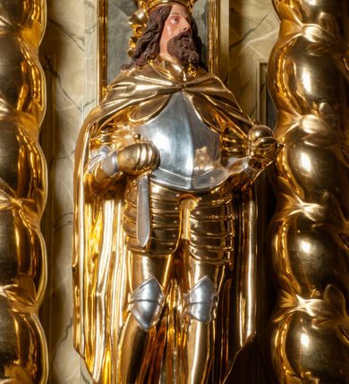 Zdjęcie nr 112: Drewniany, przyścienny ołtarz o formach architektonicznych, jednoosiowy, jednokondygnacyjny ze zwieńczeniem. Mensa murowana w kształcie prostopadłościanu zwieńczonego profilowanym gzymsem; antepedium prostokątne, w drewnianej, płaskorzeźbionej w motywy akantowe, złoconej ramie, dwustronne. Awers tłoczony, srebrzony, wykonany w technice papier mâché; rewers z malowanym na desce wyobrażeniem Veraicon na tle narzędzi męki. Tabernakulum na osi, złożone z mosiężnej, złoconej, sześciobocznej skrzynki w rozbudowanej, drewnianej obudowie o formach architektonicznych. Na nim tron wystawienia w kształcie niszy dekorowanej kratką, nakrytej kopułką z latarnią i przysłoniętej złapanymi po bokach kotarami. Na latarni rzeźbione przedstawienie pelikana karmiącego pisklęta własną krwią. Skrzynkę z tronem ulokowano na tle parawanu ustawionego na podwójnym cokole, ażurowego w górnej części, wypełnionego dekoracją roślinną, złączonego z kopułka spływami. 
Retabulum ołtarzowe drewniane wsparte na wysokim, dwudzielnym, murowanym cokole. Cokół w obudowie drewnianej, jego kondygnacje wydzielone wydatnymi, silnie występującymi przed lico gzymsami; mocno wysunięte ku przodowi części przednie. Ich lica z prostokątnymi płycinami mieszczącymi suchy akant; w części środkowej drugiej kondygnacji cokołu, dodatkowo pełnoplastyczne główki puttów. Na cokole ustawione zdwojone, złocone kolumny o skręconych trzonach i kompozytowych kapitelach. Pomiędzy nimi płyciny wypełnione dekoracją w formie podwieszonego wieńca, u jego szczytu putta pełniące rolę atlantów. Na tle płycin ustawione drewniane, złocone figury z lewej św. Zygmunta i z prawej św. Marii Magdaleny – patronów kościoła. Pole ołtarza z prostokątną niszą zamkniętą łukiem wyniesionym; ujętą płaskorzeźbioną, złoconą ramą zdobioną suchym akantem. W niszy pełnoplastyczny, polichromowany i złocony krucyfiks na aksamitnym tle, flankowany przez płaskorzeźbione wyobrażenia słońca i księżyca. Nisza zasuwana obrazem z Przemienieniem na górze Tabor, w drewnianej, złoconej sukience. Kolumny dźwigają pełne, wyłamane na osiach podpór belkowanie, z wydatnym, silnie profilowanym gzymsem; na jego osi złocony monogram „IHS” w otoku ze srebrzonych obłoków na tle promienistej glorii. Całość wieńczą fragmenty przerwanego przyczółka o formach wklęsło-wypukłych, z ażurową dekoracją z suchego akantu. Pomiędzy ramionami przyczółka złocona gloria promienista, w centrum której płaskorzeźbiona postać Boga Ojca siedzącego na srebrzonym obłoku ze srebrzoną gołębicą Ducha Świętego u stóp. Na ramionach glorii uskrzydlone główki puttów, niektóre na tle obłoków. Po bokach, na gzymsie siedzące postaci nagich, adorujących puttów. Ołtarz ujęty ażurowymi, złoconymi uszami z suchego akantu, w który wplecione są groteskowe putta trzymające pochodnie. Większość powierzchni ołtarza marmoryzowana, w kolorze jasnej, oliwkowej zieleni, z ciemniejszymi brązowymi elementami wypełniającymi płyciny. Złocenia w partiach ornamentów, kolumn oraz załamaniach profili elementów architektonicznych; srebrzone obłoki, części szat postaci i pelikan. 