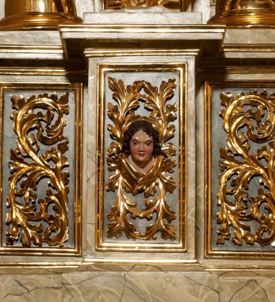 Zdjęcie nr 15: Drewniany, przyścienny ołtarz o formach architektonicznych, jednoosiowy, jednokondygnacyjny ze zwieńczeniem. Mensa murowana w kształcie prostopadłościanu zwieńczonego profilowanym gzymsem; antepedium prostokątne, w drewnianej, płaskorzeźbionej w motywy akantowe, złoconej ramie, dwustronne. Awers tłoczony, srebrzony, wykonany w technice papier mâché; rewers z malowanym na desce wyobrażeniem Veraicon na tle narzędzi męki. Tabernakulum na osi, złożone z mosiężnej, złoconej, sześciobocznej skrzynki w rozbudowanej, drewnianej obudowie o formach architektonicznych. Na nim tron wystawienia w kształcie niszy dekorowanej kratką, nakrytej kopułką z latarnią i przysłoniętej złapanymi po bokach kotarami. Na latarni rzeźbione przedstawienie pelikana karmiącego pisklęta własną krwią. Skrzynkę z tronem ulokowano na tle parawanu ustawionego na podwójnym cokole, ażurowego w górnej części, wypełnionego dekoracją roślinną, złączonego z kopułka spływami. 
Retabulum ołtarzowe drewniane wsparte na wysokim, dwudzielnym, murowanym cokole. Cokół w obudowie drewnianej, jego kondygnacje wydzielone wydatnymi, silnie występującymi przed lico gzymsami; mocno wysunięte ku przodowi części przednie. Ich lica z prostokątnymi płycinami mieszczącymi suchy akant; w części środkowej drugiej kondygnacji cokołu, dodatkowo pełnoplastyczne główki puttów. Na cokole ustawione zdwojone, złocone kolumny o skręconych trzonach i kompozytowych kapitelach. Pomiędzy nimi płyciny wypełnione dekoracją w formie podwieszonego wieńca, u jego szczytu putta pełniące rolę atlantów. Na tle płycin ustawione drewniane, złocone figury z lewej św. Zygmunta i z prawej św. Marii Magdaleny – patronów kościoła. Pole ołtarza z prostokątną niszą zamkniętą łukiem wyniesionym; ujętą płaskorzeźbioną, złoconą ramą zdobioną suchym akantem. W niszy pełnoplastyczny, polichromowany i złocony krucyfiks na aksamitnym tle, flankowany przez płaskorzeźbione wyobrażenia słońca i księżyca. Nisza zasuwana obrazem z Przemienieniem na górze Tabor, w drewnianej, złoconej sukience. Kolumny dźwigają pełne, wyłamane na osiach podpór belkowanie, z wydatnym, silnie profilowanym gzymsem; na jego osi złocony monogram „IHS” w otoku ze srebrzonych obłoków na tle promienistej glorii. Całość wieńczą fragmenty przerwanego przyczółka o formach wklęsło-wypukłych, z ażurową dekoracją z suchego akantu. Pomiędzy ramionami przyczółka złocona gloria promienista, w centrum której płaskorzeźbiona postać Boga Ojca siedzącego na srebrzonym obłoku ze srebrzoną gołębicą Ducha Świętego u stóp. Na ramionach glorii uskrzydlone główki puttów, niektóre na tle obłoków. Po bokach, na gzymsie siedzące postaci nagich, adorujących puttów. Ołtarz ujęty ażurowymi, złoconymi uszami z suchego akantu, w który wplecione są groteskowe putta trzymające pochodnie. Większość powierzchni ołtarza marmoryzowana, w kolorze jasnej, oliwkowej zieleni, z ciemniejszymi brązowymi elementami wypełniającymi płyciny. Złocenia w partiach ornamentów, kolumn oraz załamaniach profili elementów architektonicznych; srebrzone obłoki, części szat postaci i pelikan. 