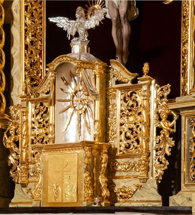 Zdjęcie nr 3: Drewniany, przyścienny ołtarz o formach architektonicznych, jednoosiowy, jednokondygnacyjny ze zwieńczeniem. Mensa murowana w kształcie prostopadłościanu zwieńczonego profilowanym gzymsem; antepedium prostokątne, w drewnianej, płaskorzeźbionej w motywy akantowe, złoconej ramie, dwustronne. Awers tłoczony, srebrzony, wykonany w technice papier mâché; rewers z malowanym na desce wyobrażeniem Veraicon na tle narzędzi męki. Tabernakulum na osi, złożone z mosiężnej, złoconej, sześciobocznej skrzynki w rozbudowanej, drewnianej obudowie o formach architektonicznych. Na nim tron wystawienia w kształcie niszy dekorowanej kratką, nakrytej kopułką z latarnią i przysłoniętej złapanymi po bokach kotarami. Na latarni rzeźbione przedstawienie pelikana karmiącego pisklęta własną krwią. Skrzynkę z tronem ulokowano na tle parawanu ustawionego na podwójnym cokole, ażurowego w górnej części, wypełnionego dekoracją roślinną, złączonego z kopułka spływami. 
Retabulum ołtarzowe drewniane wsparte na wysokim, dwudzielnym, murowanym cokole. Cokół w obudowie drewnianej, jego kondygnacje wydzielone wydatnymi, silnie występującymi przed lico gzymsami; mocno wysunięte ku przodowi części przednie. Ich lica z prostokątnymi płycinami mieszczącymi suchy akant; w części środkowej drugiej kondygnacji cokołu, dodatkowo pełnoplastyczne główki puttów. Na cokole ustawione zdwojone, złocone kolumny o skręconych trzonach i kompozytowych kapitelach. Pomiędzy nimi płyciny wypełnione dekoracją w formie podwieszonego wieńca, u jego szczytu putta pełniące rolę atlantów. Na tle płycin ustawione drewniane, złocone figury z lewej św. Zygmunta i z prawej św. Marii Magdaleny – patronów kościoła. Pole ołtarza z prostokątną niszą zamkniętą łukiem wyniesionym; ujętą płaskorzeźbioną, złoconą ramą zdobioną suchym akantem. W niszy pełnoplastyczny, polichromowany i złocony krucyfiks na aksamitnym tle, flankowany przez płaskorzeźbione wyobrażenia słońca i księżyca. Nisza zasuwana obrazem z Przemienieniem na górze Tabor, w drewnianej, złoconej sukience. Kolumny dźwigają pełne, wyłamane na osiach podpór belkowanie, z wydatnym, silnie profilowanym gzymsem; na jego osi złocony monogram „IHS” w otoku ze srebrzonych obłoków na tle promienistej glorii. Całość wieńczą fragmenty przerwanego przyczółka o formach wklęsło-wypukłych, z ażurową dekoracją z suchego akantu. Pomiędzy ramionami przyczółka złocona gloria promienista, w centrum której płaskorzeźbiona postać Boga Ojca siedzącego na srebrzonym obłoku ze srebrzoną gołębicą Ducha Świętego u stóp. Na ramionach glorii uskrzydlone główki puttów, niektóre na tle obłoków. Po bokach, na gzymsie siedzące postaci nagich, adorujących puttów. Ołtarz ujęty ażurowymi, złoconymi uszami z suchego akantu, w który wplecione są groteskowe putta trzymające pochodnie. Większość powierzchni ołtarza marmoryzowana, w kolorze jasnej, oliwkowej zieleni, z ciemniejszymi brązowymi elementami wypełniającymi płyciny. Złocenia w partiach ornamentów, kolumn oraz załamaniach profili elementów architektonicznych; srebrzone obłoki, części szat postaci i pelikan. 