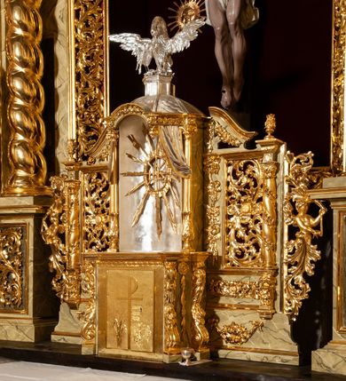 Zdjęcie nr 2: Drewniany, przyścienny ołtarz o formach architektonicznych, jednoosiowy, jednokondygnacyjny ze zwieńczeniem. Mensa murowana w kształcie prostopadłościanu zwieńczonego profilowanym gzymsem; antepedium prostokątne, w drewnianej, płaskorzeźbionej w motywy akantowe, złoconej ramie, dwustronne. Awers tłoczony, srebrzony, wykonany w technice papier mâché; rewers z malowanym na desce wyobrażeniem Veraicon na tle narzędzi męki. Tabernakulum na osi, złożone z mosiężnej, złoconej, sześciobocznej skrzynki w rozbudowanej, drewnianej obudowie o formach architektonicznych. Na nim tron wystawienia w kształcie niszy dekorowanej kratką, nakrytej kopułką z latarnią i przysłoniętej złapanymi po bokach kotarami. Na latarni rzeźbione przedstawienie pelikana karmiącego pisklęta własną krwią. Skrzynkę z tronem ulokowano na tle parawanu ustawionego na podwójnym cokole, ażurowego w górnej części, wypełnionego dekoracją roślinną, złączonego z kopułka spływami. 
Retabulum ołtarzowe drewniane wsparte na wysokim, dwudzielnym, murowanym cokole. Cokół w obudowie drewnianej, jego kondygnacje wydzielone wydatnymi, silnie występującymi przed lico gzymsami; mocno wysunięte ku przodowi części przednie. Ich lica z prostokątnymi płycinami mieszczącymi suchy akant; w części środkowej drugiej kondygnacji cokołu, dodatkowo pełnoplastyczne główki puttów. Na cokole ustawione zdwojone, złocone kolumny o skręconych trzonach i kompozytowych kapitelach. Pomiędzy nimi płyciny wypełnione dekoracją w formie podwieszonego wieńca, u jego szczytu putta pełniące rolę atlantów. Na tle płycin ustawione drewniane, złocone figury z lewej św. Zygmunta i z prawej św. Marii Magdaleny – patronów kościoła. Pole ołtarza z prostokątną niszą zamkniętą łukiem wyniesionym; ujętą płaskorzeźbioną, złoconą ramą zdobioną suchym akantem. W niszy pełnoplastyczny, polichromowany i złocony krucyfiks na aksamitnym tle, flankowany przez płaskorzeźbione wyobrażenia słońca i księżyca. Nisza zasuwana obrazem z Przemienieniem na górze Tabor, w drewnianej, złoconej sukience. Kolumny dźwigają pełne, wyłamane na osiach podpór belkowanie, z wydatnym, silnie profilowanym gzymsem; na jego osi złocony monogram „IHS” w otoku ze srebrzonych obłoków na tle promienistej glorii. Całość wieńczą fragmenty przerwanego przyczółka o formach wklęsło-wypukłych, z ażurową dekoracją z suchego akantu. Pomiędzy ramionami przyczółka złocona gloria promienista, w centrum której płaskorzeźbiona postać Boga Ojca siedzącego na srebrzonym obłoku ze srebrzoną gołębicą Ducha Świętego u stóp. Na ramionach glorii uskrzydlone główki puttów, niektóre na tle obłoków. Po bokach, na gzymsie siedzące postaci nagich, adorujących puttów. Ołtarz ujęty ażurowymi, złoconymi uszami z suchego akantu, w który wplecione są groteskowe putta trzymające pochodnie. Większość powierzchni ołtarza marmoryzowana, w kolorze jasnej, oliwkowej zieleni, z ciemniejszymi brązowymi elementami wypełniającymi płyciny. Złocenia w partiach ornamentów, kolumn oraz załamaniach profili elementów architektonicznych; srebrzone obłoki, części szat postaci i pelikan. 