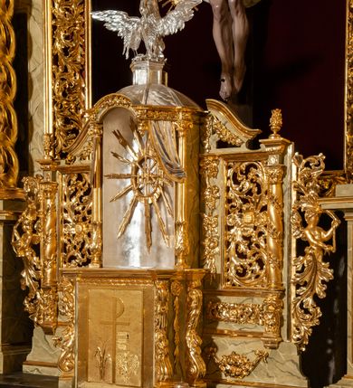 Zdjęcie nr 114: Drewniany, przyścienny ołtarz o formach architektonicznych, jednoosiowy, jednokondygnacyjny ze zwieńczeniem. Mensa murowana w kształcie prostopadłościanu zwieńczonego profilowanym gzymsem; antepedium prostokątne, w drewnianej, płaskorzeźbionej w motywy akantowe, złoconej ramie, dwustronne. Awers tłoczony, srebrzony, wykonany w technice papier mâché; rewers z malowanym na desce wyobrażeniem Veraicon na tle narzędzi męki. Tabernakulum na osi, złożone z mosiężnej, złoconej, sześciobocznej skrzynki w rozbudowanej, drewnianej obudowie o formach architektonicznych. Na nim tron wystawienia w kształcie niszy dekorowanej kratką, nakrytej kopułką z latarnią i przysłoniętej złapanymi po bokach kotarami. Na latarni rzeźbione przedstawienie pelikana karmiącego pisklęta własną krwią. Skrzynkę z tronem ulokowano na tle parawanu ustawionego na podwójnym cokole, ażurowego w górnej części, wypełnionego dekoracją roślinną, złączonego z kopułka spływami. 
Retabulum ołtarzowe drewniane wsparte na wysokim, dwudzielnym, murowanym cokole. Cokół w obudowie drewnianej, jego kondygnacje wydzielone wydatnymi, silnie występującymi przed lico gzymsami; mocno wysunięte ku przodowi części przednie. Ich lica z prostokątnymi płycinami mieszczącymi suchy akant; w części środkowej drugiej kondygnacji cokołu, dodatkowo pełnoplastyczne główki puttów. Na cokole ustawione zdwojone, złocone kolumny o skręconych trzonach i kompozytowych kapitelach. Pomiędzy nimi płyciny wypełnione dekoracją w formie podwieszonego wieńca, u jego szczytu putta pełniące rolę atlantów. Na tle płycin ustawione drewniane, złocone figury z lewej św. Zygmunta i z prawej św. Marii Magdaleny – patronów kościoła. Pole ołtarza z prostokątną niszą zamkniętą łukiem wyniesionym; ujętą płaskorzeźbioną, złoconą ramą zdobioną suchym akantem. W niszy pełnoplastyczny, polichromowany i złocony krucyfiks na aksamitnym tle, flankowany przez płaskorzeźbione wyobrażenia słońca i księżyca. Nisza zasuwana obrazem z Przemienieniem na górze Tabor, w drewnianej, złoconej sukience. Kolumny dźwigają pełne, wyłamane na osiach podpór belkowanie, z wydatnym, silnie profilowanym gzymsem; na jego osi złocony monogram „IHS” w otoku ze srebrzonych obłoków na tle promienistej glorii. Całość wieńczą fragmenty przerwanego przyczółka o formach wklęsło-wypukłych, z ażurową dekoracją z suchego akantu. Pomiędzy ramionami przyczółka złocona gloria promienista, w centrum której płaskorzeźbiona postać Boga Ojca siedzącego na srebrzonym obłoku ze srebrzoną gołębicą Ducha Świętego u stóp. Na ramionach glorii uskrzydlone główki puttów, niektóre na tle obłoków. Po bokach, na gzymsie siedzące postaci nagich, adorujących puttów. Ołtarz ujęty ażurowymi, złoconymi uszami z suchego akantu, w który wplecione są groteskowe putta trzymające pochodnie. Większość powierzchni ołtarza marmoryzowana, w kolorze jasnej, oliwkowej zieleni, z ciemniejszymi brązowymi elementami wypełniającymi płyciny. Złocenia w partiach ornamentów, kolumn oraz załamaniach profili elementów architektonicznych; srebrzone obłoki, części szat postaci i pelikan. 