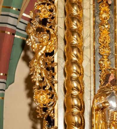 Zdjęcie nr 22: Drewniany, przyścienny ołtarz o formach architektonicznych, jednoosiowy, jednokondygnacyjny ze zwieńczeniem. Mensa murowana w kształcie prostopadłościanu zwieńczonego profilowanym gzymsem; antepedium prostokątne, w drewnianej, płaskorzeźbionej w motywy akantowe, złoconej ramie, dwustronne. Awers tłoczony, srebrzony, wykonany w technice papier mâché; rewers z malowanym na desce wyobrażeniem Veraicon na tle narzędzi męki. Tabernakulum na osi, złożone z mosiężnej, złoconej, sześciobocznej skrzynki w rozbudowanej, drewnianej obudowie o formach architektonicznych. Na nim tron wystawienia w kształcie niszy dekorowanej kratką, nakrytej kopułką z latarnią i przysłoniętej złapanymi po bokach kotarami. Na latarni rzeźbione przedstawienie pelikana karmiącego pisklęta własną krwią. Skrzynkę z tronem ulokowano na tle parawanu ustawionego na podwójnym cokole, ażurowego w górnej części, wypełnionego dekoracją roślinną, złączonego z kopułka spływami. 
Retabulum ołtarzowe drewniane wsparte na wysokim, dwudzielnym, murowanym cokole. Cokół w obudowie drewnianej, jego kondygnacje wydzielone wydatnymi, silnie występującymi przed lico gzymsami; mocno wysunięte ku przodowi części przednie. Ich lica z prostokątnymi płycinami mieszczącymi suchy akant; w części środkowej drugiej kondygnacji cokołu, dodatkowo pełnoplastyczne główki puttów. Na cokole ustawione zdwojone, złocone kolumny o skręconych trzonach i kompozytowych kapitelach. Pomiędzy nimi płyciny wypełnione dekoracją w formie podwieszonego wieńca, u jego szczytu putta pełniące rolę atlantów. Na tle płycin ustawione drewniane, złocone figury z lewej św. Zygmunta i z prawej św. Marii Magdaleny – patronów kościoła. Pole ołtarza z prostokątną niszą zamkniętą łukiem wyniesionym; ujętą płaskorzeźbioną, złoconą ramą zdobioną suchym akantem. W niszy pełnoplastyczny, polichromowany i złocony krucyfiks na aksamitnym tle, flankowany przez płaskorzeźbione wyobrażenia słońca i księżyca. Nisza zasuwana obrazem z Przemienieniem na górze Tabor, w drewnianej, złoconej sukience. Kolumny dźwigają pełne, wyłamane na osiach podpór belkowanie, z wydatnym, silnie profilowanym gzymsem; na jego osi złocony monogram „IHS” w otoku ze srebrzonych obłoków na tle promienistej glorii. Całość wieńczą fragmenty przerwanego przyczółka o formach wklęsło-wypukłych, z ażurową dekoracją z suchego akantu. Pomiędzy ramionami przyczółka złocona gloria promienista, w centrum której płaskorzeźbiona postać Boga Ojca siedzącego na srebrzonym obłoku ze srebrzoną gołębicą Ducha Świętego u stóp. Na ramionach glorii uskrzydlone główki puttów, niektóre na tle obłoków. Po bokach, na gzymsie siedzące postaci nagich, adorujących puttów. Ołtarz ujęty ażurowymi, złoconymi uszami z suchego akantu, w który wplecione są groteskowe putta trzymające pochodnie. Większość powierzchni ołtarza marmoryzowana, w kolorze jasnej, oliwkowej zieleni, z ciemniejszymi brązowymi elementami wypełniającymi płyciny. Złocenia w partiach ornamentów, kolumn oraz załamaniach profili elementów architektonicznych; srebrzone obłoki, części szat postaci i pelikan. 