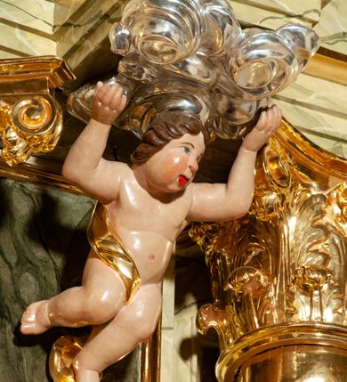 Zdjęcie nr 25: Drewniany, przyścienny ołtarz o formach architektonicznych, jednoosiowy, jednokondygnacyjny ze zwieńczeniem. Mensa murowana w kształcie prostopadłościanu zwieńczonego profilowanym gzymsem; antepedium prostokątne, w drewnianej, płaskorzeźbionej w motywy akantowe, złoconej ramie, dwustronne. Awers tłoczony, srebrzony, wykonany w technice papier mâché; rewers z malowanym na desce wyobrażeniem Veraicon na tle narzędzi męki. Tabernakulum na osi, złożone z mosiężnej, złoconej, sześciobocznej skrzynki w rozbudowanej, drewnianej obudowie o formach architektonicznych. Na nim tron wystawienia w kształcie niszy dekorowanej kratką, nakrytej kopułką z latarnią i przysłoniętej złapanymi po bokach kotarami. Na latarni rzeźbione przedstawienie pelikana karmiącego pisklęta własną krwią. Skrzynkę z tronem ulokowano na tle parawanu ustawionego na podwójnym cokole, ażurowego w górnej części, wypełnionego dekoracją roślinną, złączonego z kopułka spływami. 
Retabulum ołtarzowe drewniane wsparte na wysokim, dwudzielnym, murowanym cokole. Cokół w obudowie drewnianej, jego kondygnacje wydzielone wydatnymi, silnie występującymi przed lico gzymsami; mocno wysunięte ku przodowi części przednie. Ich lica z prostokątnymi płycinami mieszczącymi suchy akant; w części środkowej drugiej kondygnacji cokołu, dodatkowo pełnoplastyczne główki puttów. Na cokole ustawione zdwojone, złocone kolumny o skręconych trzonach i kompozytowych kapitelach. Pomiędzy nimi płyciny wypełnione dekoracją w formie podwieszonego wieńca, u jego szczytu putta pełniące rolę atlantów. Na tle płycin ustawione drewniane, złocone figury z lewej św. Zygmunta i z prawej św. Marii Magdaleny – patronów kościoła. Pole ołtarza z prostokątną niszą zamkniętą łukiem wyniesionym; ujętą płaskorzeźbioną, złoconą ramą zdobioną suchym akantem. W niszy pełnoplastyczny, polichromowany i złocony krucyfiks na aksamitnym tle, flankowany przez płaskorzeźbione wyobrażenia słońca i księżyca. Nisza zasuwana obrazem z Przemienieniem na górze Tabor, w drewnianej, złoconej sukience. Kolumny dźwigają pełne, wyłamane na osiach podpór belkowanie, z wydatnym, silnie profilowanym gzymsem; na jego osi złocony monogram „IHS” w otoku ze srebrzonych obłoków na tle promienistej glorii. Całość wieńczą fragmenty przerwanego przyczółka o formach wklęsło-wypukłych, z ażurową dekoracją z suchego akantu. Pomiędzy ramionami przyczółka złocona gloria promienista, w centrum której płaskorzeźbiona postać Boga Ojca siedzącego na srebrzonym obłoku ze srebrzoną gołębicą Ducha Świętego u stóp. Na ramionach glorii uskrzydlone główki puttów, niektóre na tle obłoków. Po bokach, na gzymsie siedzące postaci nagich, adorujących puttów. Ołtarz ujęty ażurowymi, złoconymi uszami z suchego akantu, w który wplecione są groteskowe putta trzymające pochodnie. Większość powierzchni ołtarza marmoryzowana, w kolorze jasnej, oliwkowej zieleni, z ciemniejszymi brązowymi elementami wypełniającymi płyciny. Złocenia w partiach ornamentów, kolumn oraz załamaniach profili elementów architektonicznych; srebrzone obłoki, części szat postaci i pelikan. 