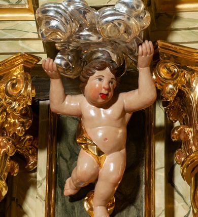 Zdjęcie nr 24: Drewniany, przyścienny ołtarz o formach architektonicznych, jednoosiowy, jednokondygnacyjny ze zwieńczeniem. Mensa murowana w kształcie prostopadłościanu zwieńczonego profilowanym gzymsem; antepedium prostokątne, w drewnianej, płaskorzeźbionej w motywy akantowe, złoconej ramie, dwustronne. Awers tłoczony, srebrzony, wykonany w technice papier mâché; rewers z malowanym na desce wyobrażeniem Veraicon na tle narzędzi męki. Tabernakulum na osi, złożone z mosiężnej, złoconej, sześciobocznej skrzynki w rozbudowanej, drewnianej obudowie o formach architektonicznych. Na nim tron wystawienia w kształcie niszy dekorowanej kratką, nakrytej kopułką z latarnią i przysłoniętej złapanymi po bokach kotarami. Na latarni rzeźbione przedstawienie pelikana karmiącego pisklęta własną krwią. Skrzynkę z tronem ulokowano na tle parawanu ustawionego na podwójnym cokole, ażurowego w górnej części, wypełnionego dekoracją roślinną, złączonego z kopułka spływami. 
Retabulum ołtarzowe drewniane wsparte na wysokim, dwudzielnym, murowanym cokole. Cokół w obudowie drewnianej, jego kondygnacje wydzielone wydatnymi, silnie występującymi przed lico gzymsami; mocno wysunięte ku przodowi części przednie. Ich lica z prostokątnymi płycinami mieszczącymi suchy akant; w części środkowej drugiej kondygnacji cokołu, dodatkowo pełnoplastyczne główki puttów. Na cokole ustawione zdwojone, złocone kolumny o skręconych trzonach i kompozytowych kapitelach. Pomiędzy nimi płyciny wypełnione dekoracją w formie podwieszonego wieńca, u jego szczytu putta pełniące rolę atlantów. Na tle płycin ustawione drewniane, złocone figury z lewej św. Zygmunta i z prawej św. Marii Magdaleny – patronów kościoła. Pole ołtarza z prostokątną niszą zamkniętą łukiem wyniesionym; ujętą płaskorzeźbioną, złoconą ramą zdobioną suchym akantem. W niszy pełnoplastyczny, polichromowany i złocony krucyfiks na aksamitnym tle, flankowany przez płaskorzeźbione wyobrażenia słońca i księżyca. Nisza zasuwana obrazem z Przemienieniem na górze Tabor, w drewnianej, złoconej sukience. Kolumny dźwigają pełne, wyłamane na osiach podpór belkowanie, z wydatnym, silnie profilowanym gzymsem; na jego osi złocony monogram „IHS” w otoku ze srebrzonych obłoków na tle promienistej glorii. Całość wieńczą fragmenty przerwanego przyczółka o formach wklęsło-wypukłych, z ażurową dekoracją z suchego akantu. Pomiędzy ramionami przyczółka złocona gloria promienista, w centrum której płaskorzeźbiona postać Boga Ojca siedzącego na srebrzonym obłoku ze srebrzoną gołębicą Ducha Świętego u stóp. Na ramionach glorii uskrzydlone główki puttów, niektóre na tle obłoków. Po bokach, na gzymsie siedzące postaci nagich, adorujących puttów. Ołtarz ujęty ażurowymi, złoconymi uszami z suchego akantu, w który wplecione są groteskowe putta trzymające pochodnie. Większość powierzchni ołtarza marmoryzowana, w kolorze jasnej, oliwkowej zieleni, z ciemniejszymi brązowymi elementami wypełniającymi płyciny. Złocenia w partiach ornamentów, kolumn oraz załamaniach profili elementów architektonicznych; srebrzone obłoki, części szat postaci i pelikan. 