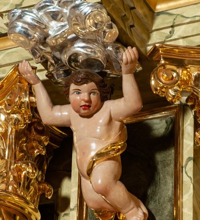 Zdjęcie nr 27: Drewniany, przyścienny ołtarz o formach architektonicznych, jednoosiowy, jednokondygnacyjny ze zwieńczeniem. Mensa murowana w kształcie prostopadłościanu zwieńczonego profilowanym gzymsem; antepedium prostokątne, w drewnianej, płaskorzeźbionej w motywy akantowe, złoconej ramie, dwustronne. Awers tłoczony, srebrzony, wykonany w technice papier mâché; rewers z malowanym na desce wyobrażeniem Veraicon na tle narzędzi męki. Tabernakulum na osi, złożone z mosiężnej, złoconej, sześciobocznej skrzynki w rozbudowanej, drewnianej obudowie o formach architektonicznych. Na nim tron wystawienia w kształcie niszy dekorowanej kratką, nakrytej kopułką z latarnią i przysłoniętej złapanymi po bokach kotarami. Na latarni rzeźbione przedstawienie pelikana karmiącego pisklęta własną krwią. Skrzynkę z tronem ulokowano na tle parawanu ustawionego na podwójnym cokole, ażurowego w górnej części, wypełnionego dekoracją roślinną, złączonego z kopułka spływami. 
Retabulum ołtarzowe drewniane wsparte na wysokim, dwudzielnym, murowanym cokole. Cokół w obudowie drewnianej, jego kondygnacje wydzielone wydatnymi, silnie występującymi przed lico gzymsami; mocno wysunięte ku przodowi części przednie. Ich lica z prostokątnymi płycinami mieszczącymi suchy akant; w części środkowej drugiej kondygnacji cokołu, dodatkowo pełnoplastyczne główki puttów. Na cokole ustawione zdwojone, złocone kolumny o skręconych trzonach i kompozytowych kapitelach. Pomiędzy nimi płyciny wypełnione dekoracją w formie podwieszonego wieńca, u jego szczytu putta pełniące rolę atlantów. Na tle płycin ustawione drewniane, złocone figury z lewej św. Zygmunta i z prawej św. Marii Magdaleny – patronów kościoła. Pole ołtarza z prostokątną niszą zamkniętą łukiem wyniesionym; ujętą płaskorzeźbioną, złoconą ramą zdobioną suchym akantem. W niszy pełnoplastyczny, polichromowany i złocony krucyfiks na aksamitnym tle, flankowany przez płaskorzeźbione wyobrażenia słońca i księżyca. Nisza zasuwana obrazem z Przemienieniem na górze Tabor, w drewnianej, złoconej sukience. Kolumny dźwigają pełne, wyłamane na osiach podpór belkowanie, z wydatnym, silnie profilowanym gzymsem; na jego osi złocony monogram „IHS” w otoku ze srebrzonych obłoków na tle promienistej glorii. Całość wieńczą fragmenty przerwanego przyczółka o formach wklęsło-wypukłych, z ażurową dekoracją z suchego akantu. Pomiędzy ramionami przyczółka złocona gloria promienista, w centrum której płaskorzeźbiona postać Boga Ojca siedzącego na srebrzonym obłoku ze srebrzoną gołębicą Ducha Świętego u stóp. Na ramionach glorii uskrzydlone główki puttów, niektóre na tle obłoków. Po bokach, na gzymsie siedzące postaci nagich, adorujących puttów. Ołtarz ujęty ażurowymi, złoconymi uszami z suchego akantu, w który wplecione są groteskowe putta trzymające pochodnie. Większość powierzchni ołtarza marmoryzowana, w kolorze jasnej, oliwkowej zieleni, z ciemniejszymi brązowymi elementami wypełniającymi płyciny. Złocenia w partiach ornamentów, kolumn oraz załamaniach profili elementów architektonicznych; srebrzone obłoki, części szat postaci i pelikan. 